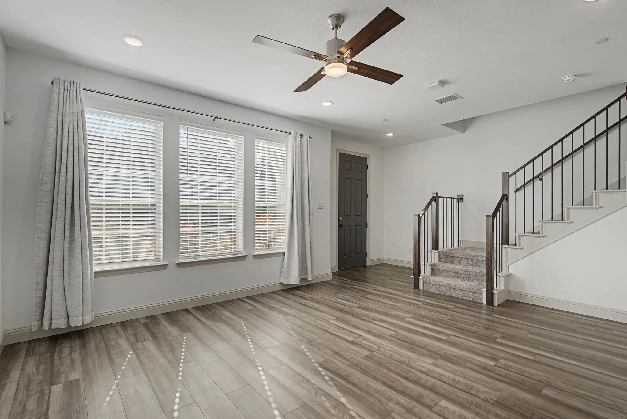 Spacious living area featuring wood-finish flooring, a contemporary ceiling fan, and recessed lighting
