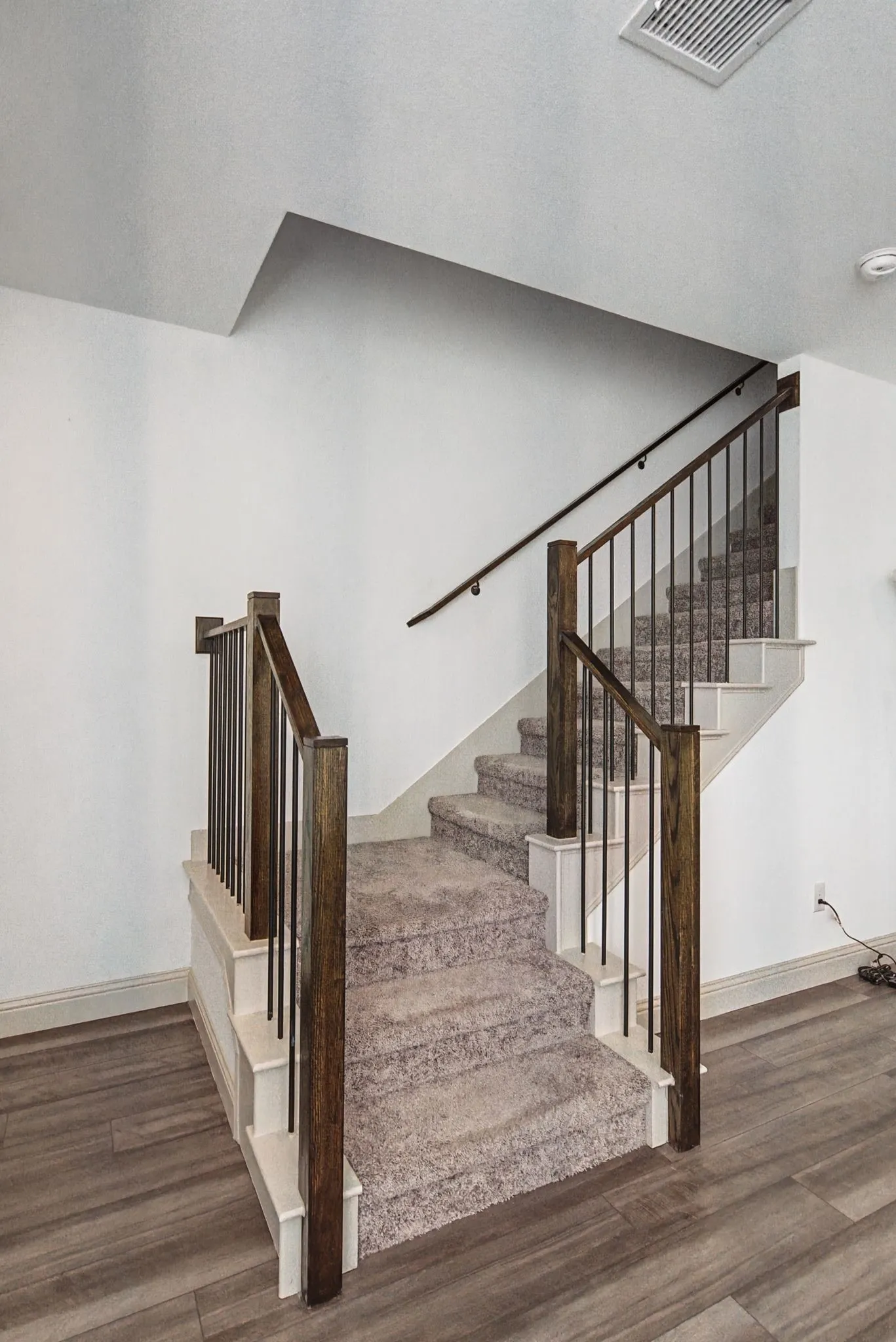 Staircase featuring dark wood newel posts and handrails, black iron balusters, and plush carpeted treads, complemented by wood-finish flooring