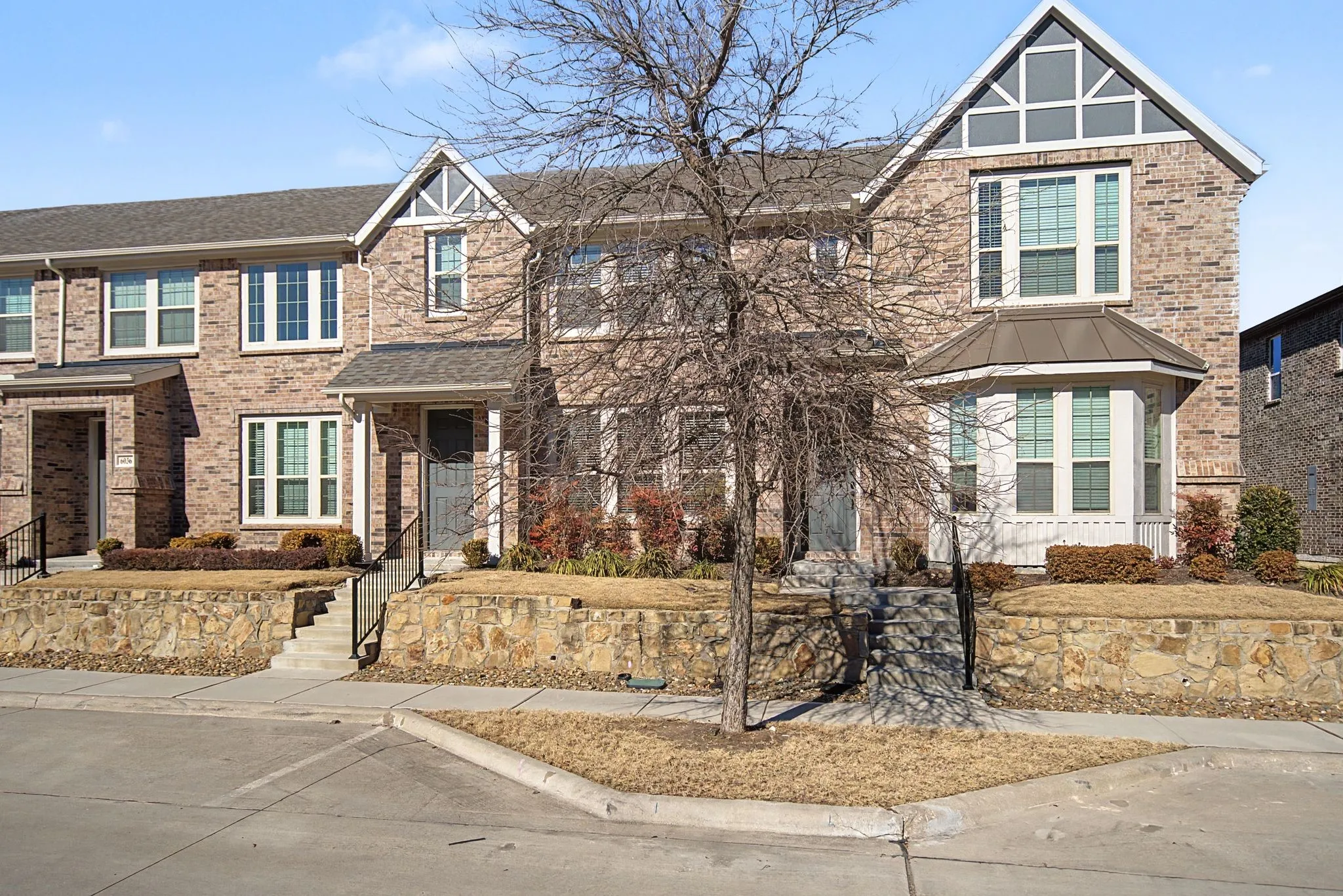 Brick townhome exterior featuring an arched gable detail, bay window, covered entry, black metal railings, and stone retaining walls