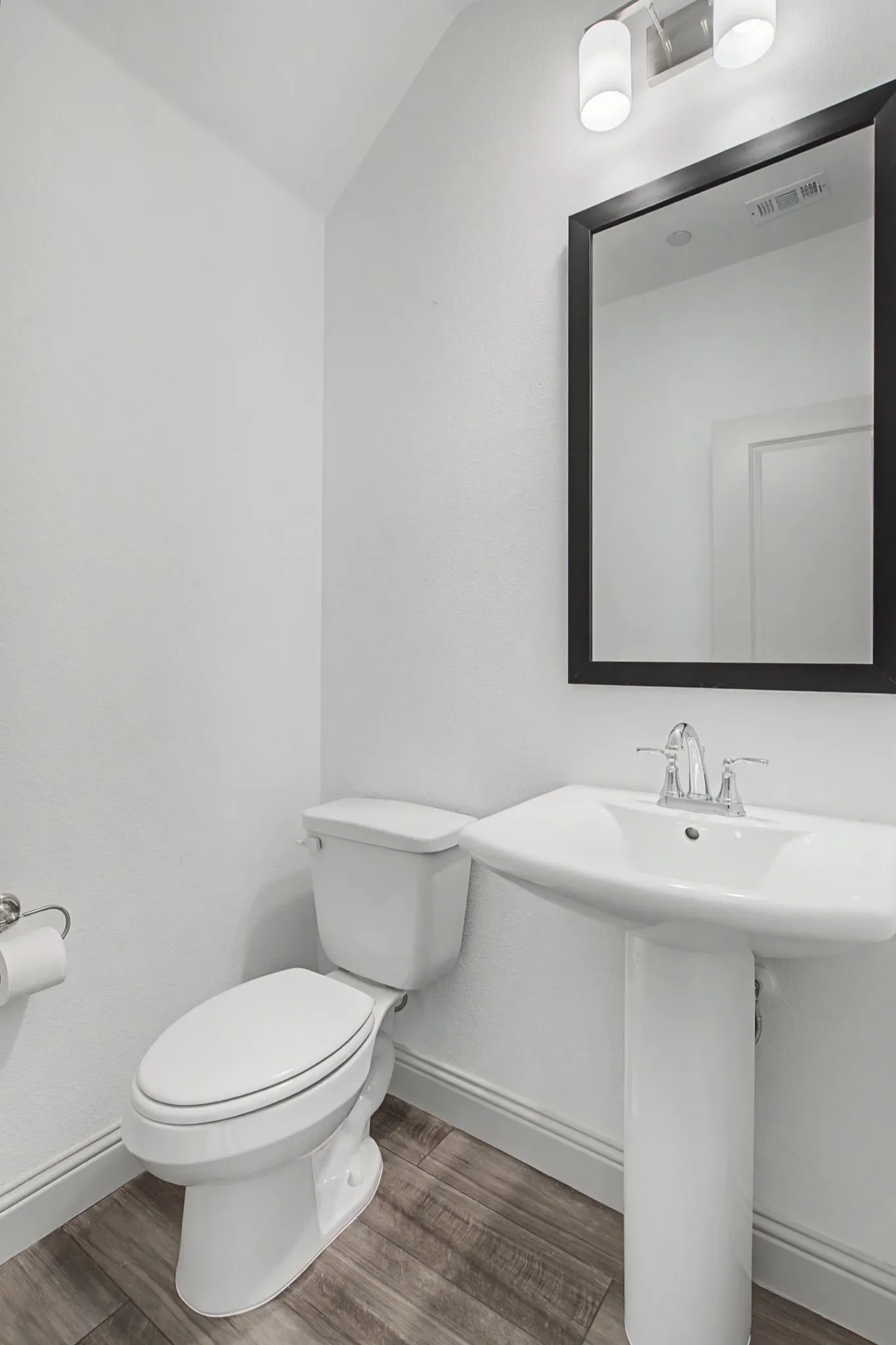 Pedestal sink with chrome faucet, framed mirror, and wood-finish flooring