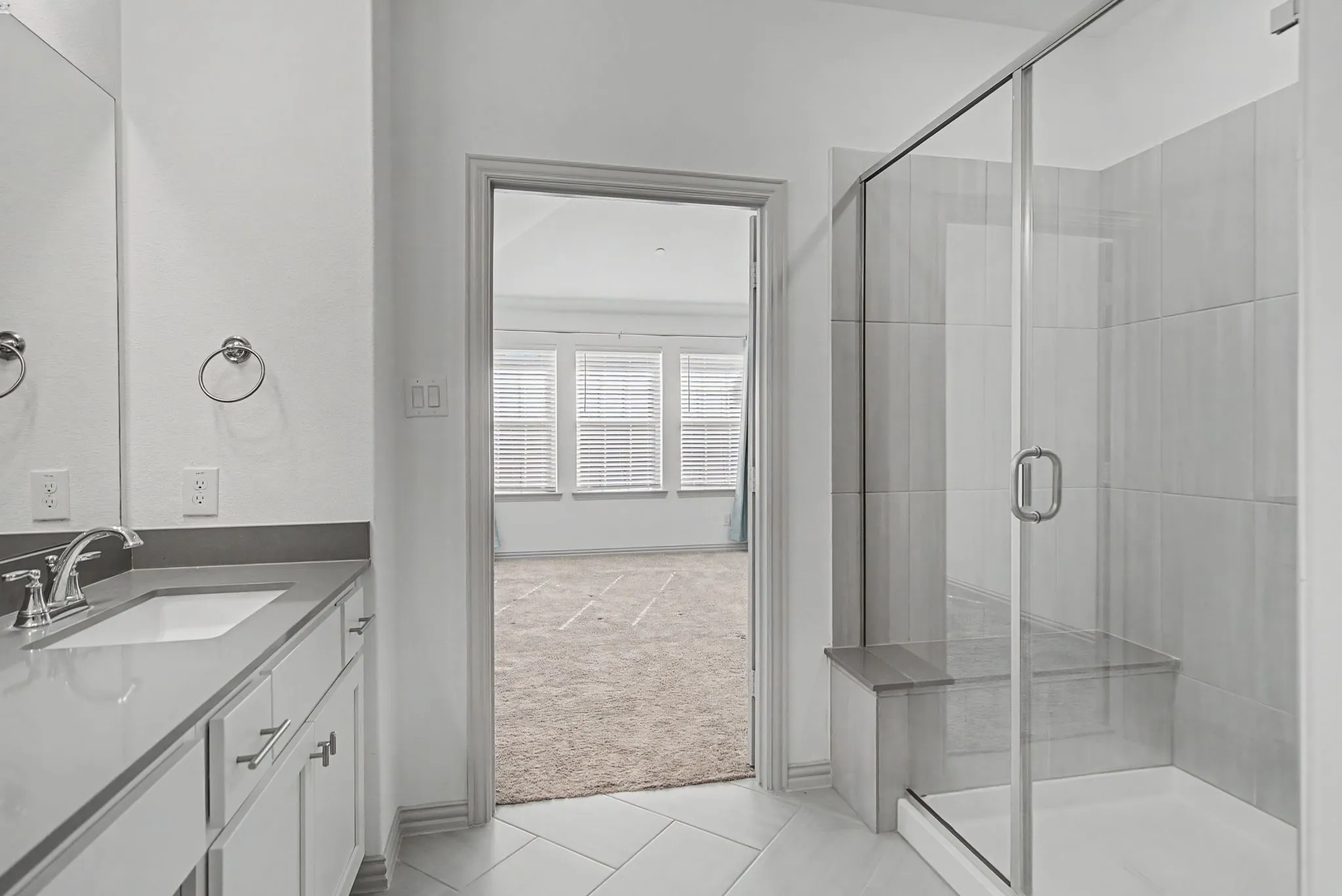 Bathroom featuring a single vanity with an undermount sink, a large wall mirror, and a glass-enclosed shower with a built-in bench