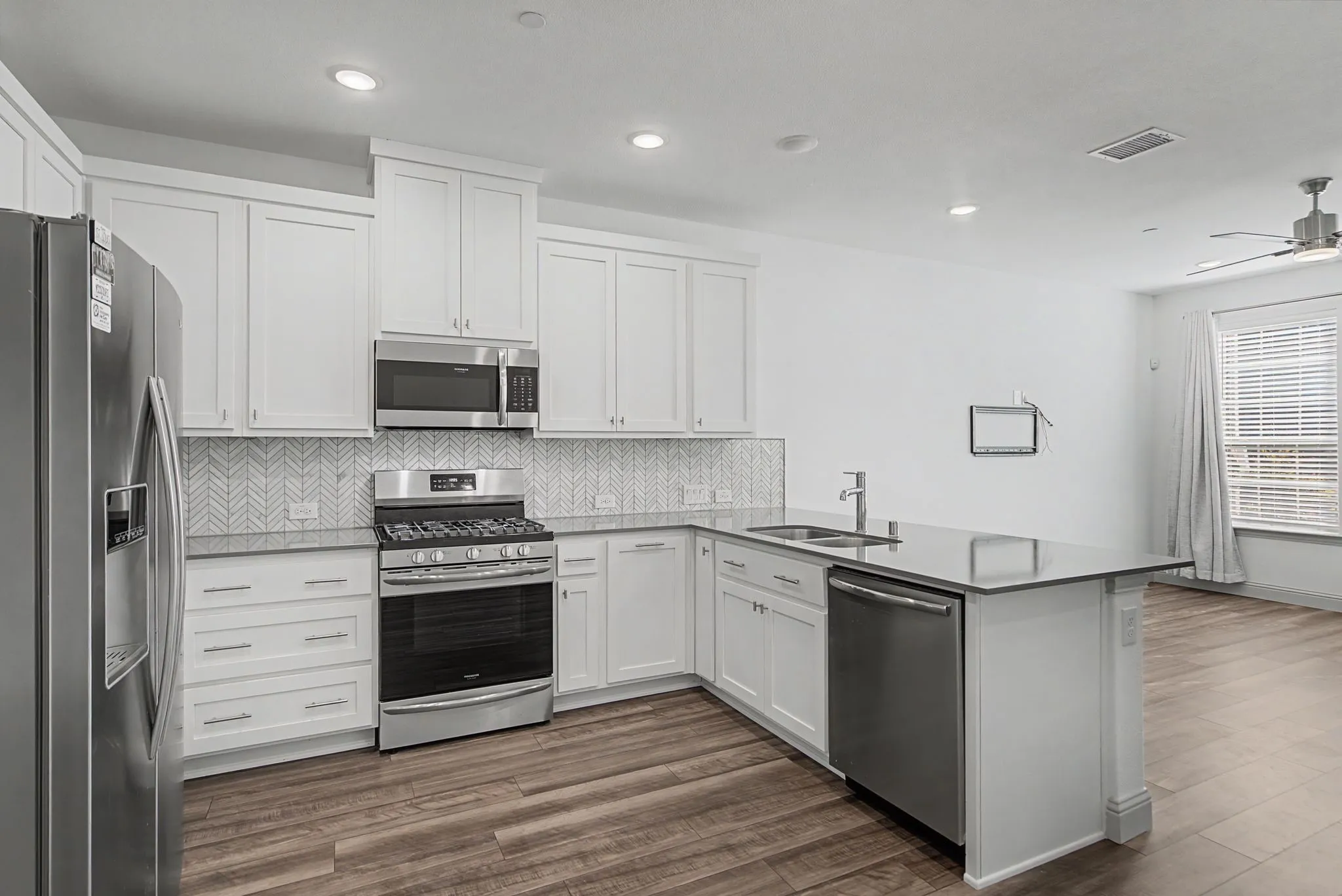 Modern kitchen featuring white shaker cabinetry, stainless steel appliances, a herringbone tile backsplash, a center island with sink, and wood-finish flooring