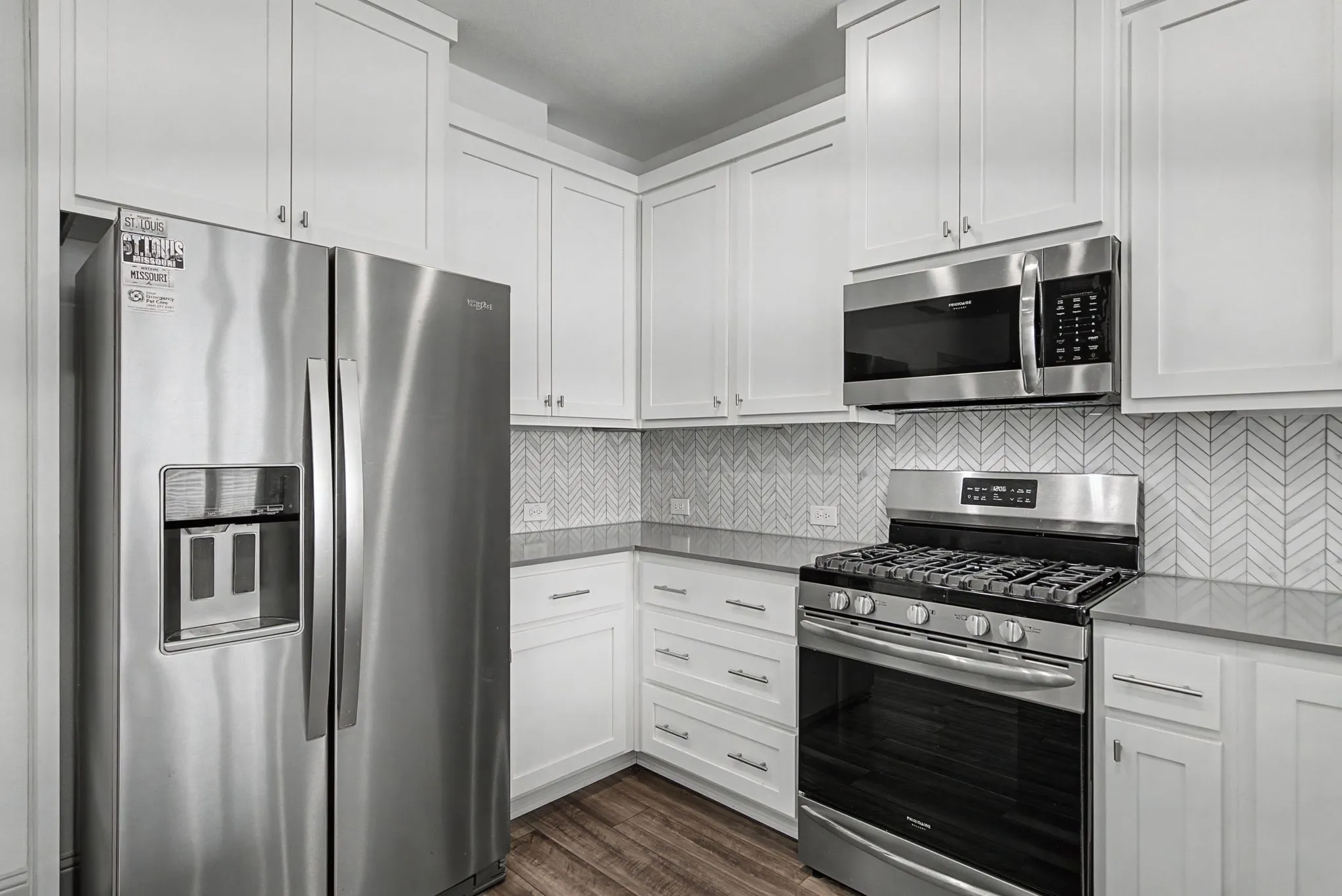 Contemporary kitchen featuring white shaker cabinetry, stainless steel appliances, a herringbone tile backsplash, and wood-finish flooring