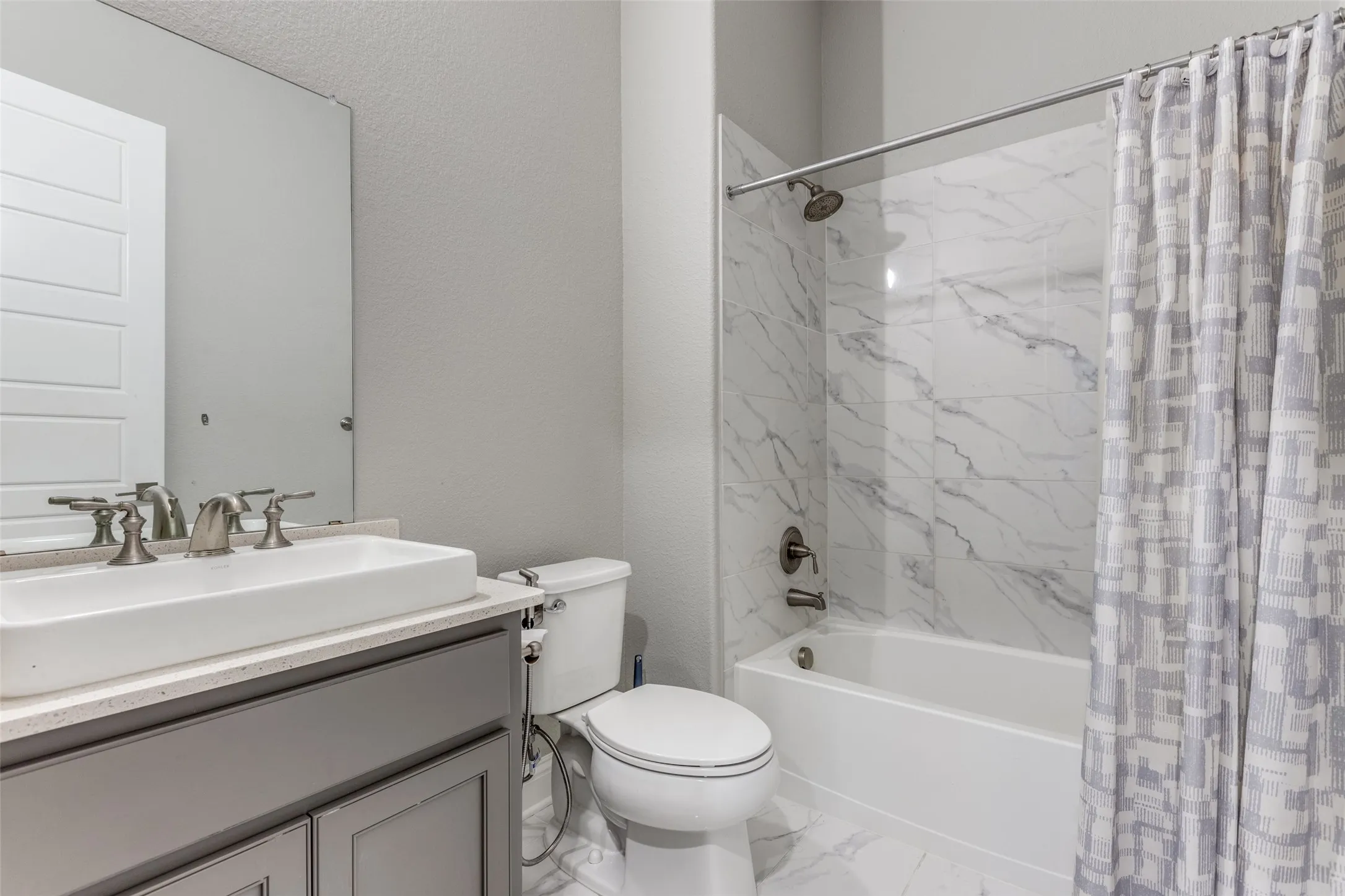 Full bathroom featuring a rectangular vessel sink, gray vanity with cabinetry, and a bathtub with a tiled surround