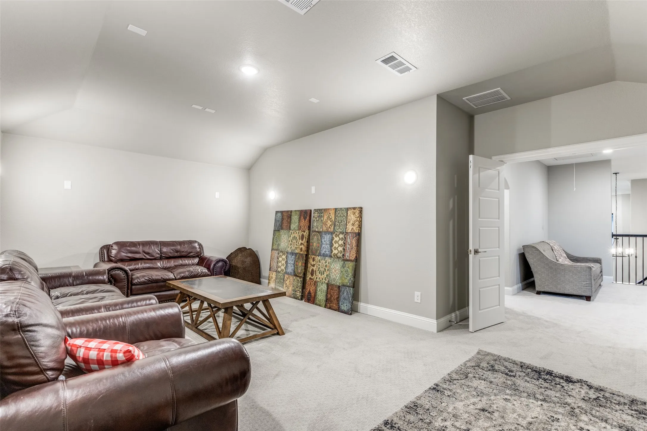 Spacious bonus room featuring vaulted ceilings, recessed lighting, neutral carpeting, and a doorway to a separate area with an iron spindle railing