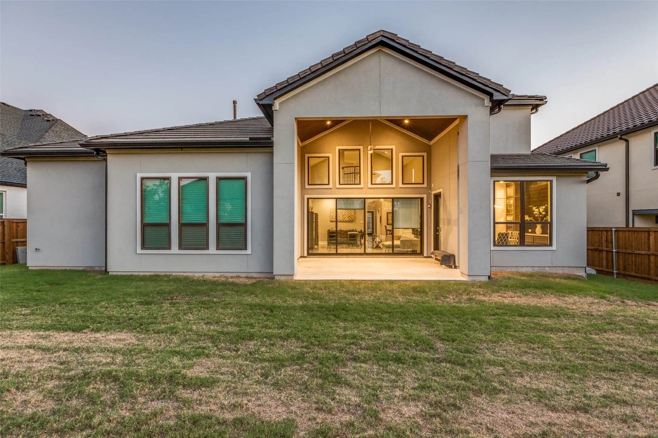 Modern stucco exterior featuring a covered patio, expansive sliding glass doors, and a vaulted ceiling with accent windows