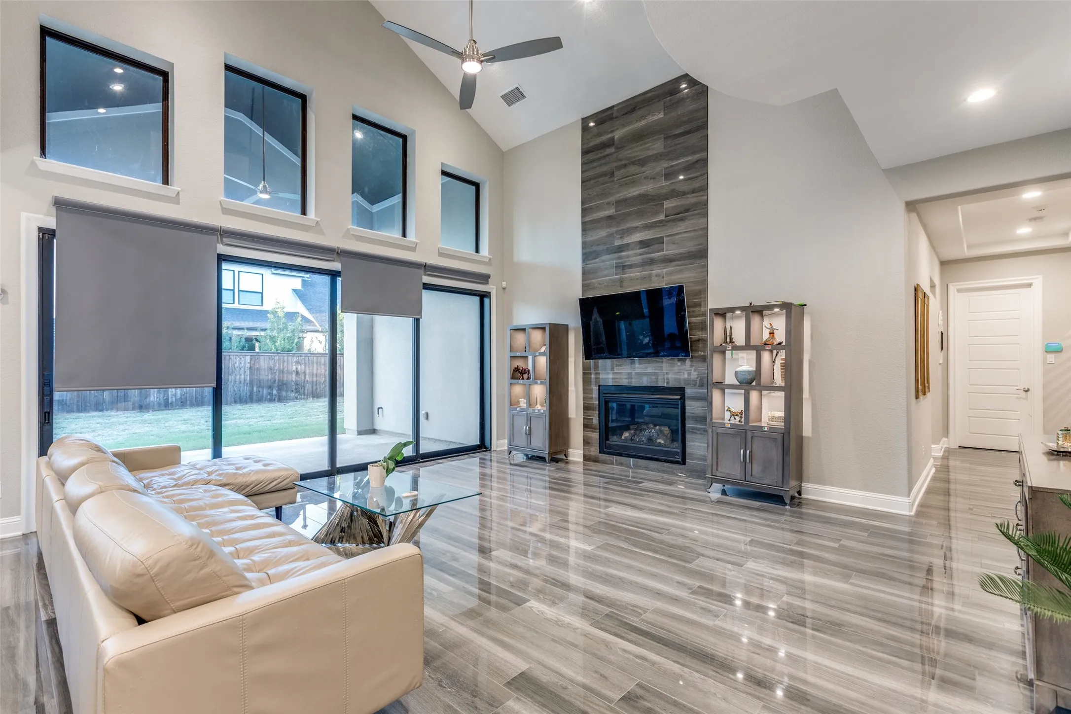Vaulted ceiling great room featuring a floor-to-ceiling accent wall with a built-in fireplace, wood-finish flooring, and a ceiling fan