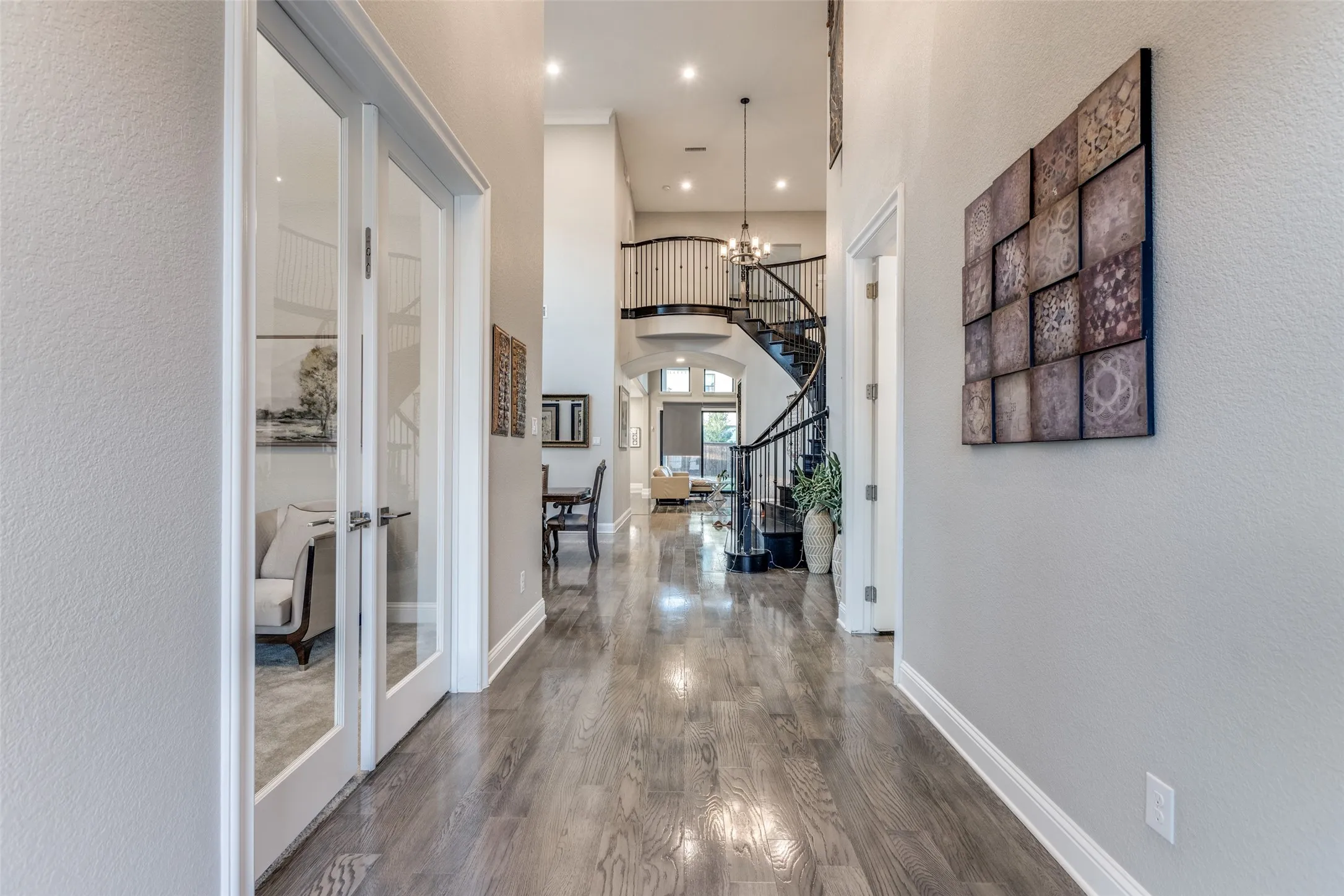 Expansive entryway featuring wood-finish flooring, recessed lighting, double glass-paneled doors, a grand curved staircase with wrought iron balusters, and high ceilings