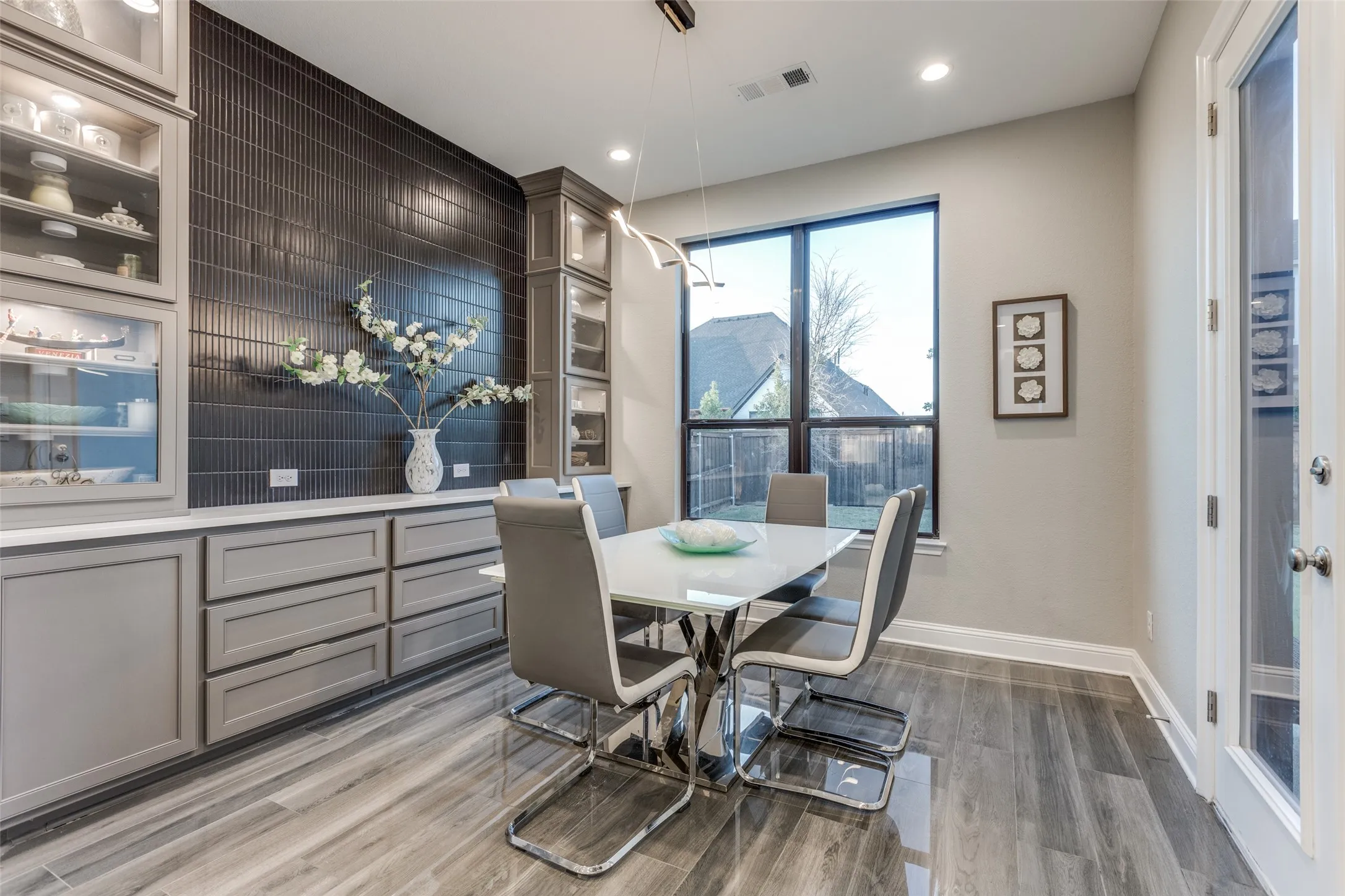 Dining area featuring a dark tile accent wall, built-in cabinetry with glass display fronts, a large window, and wood-finish flooring