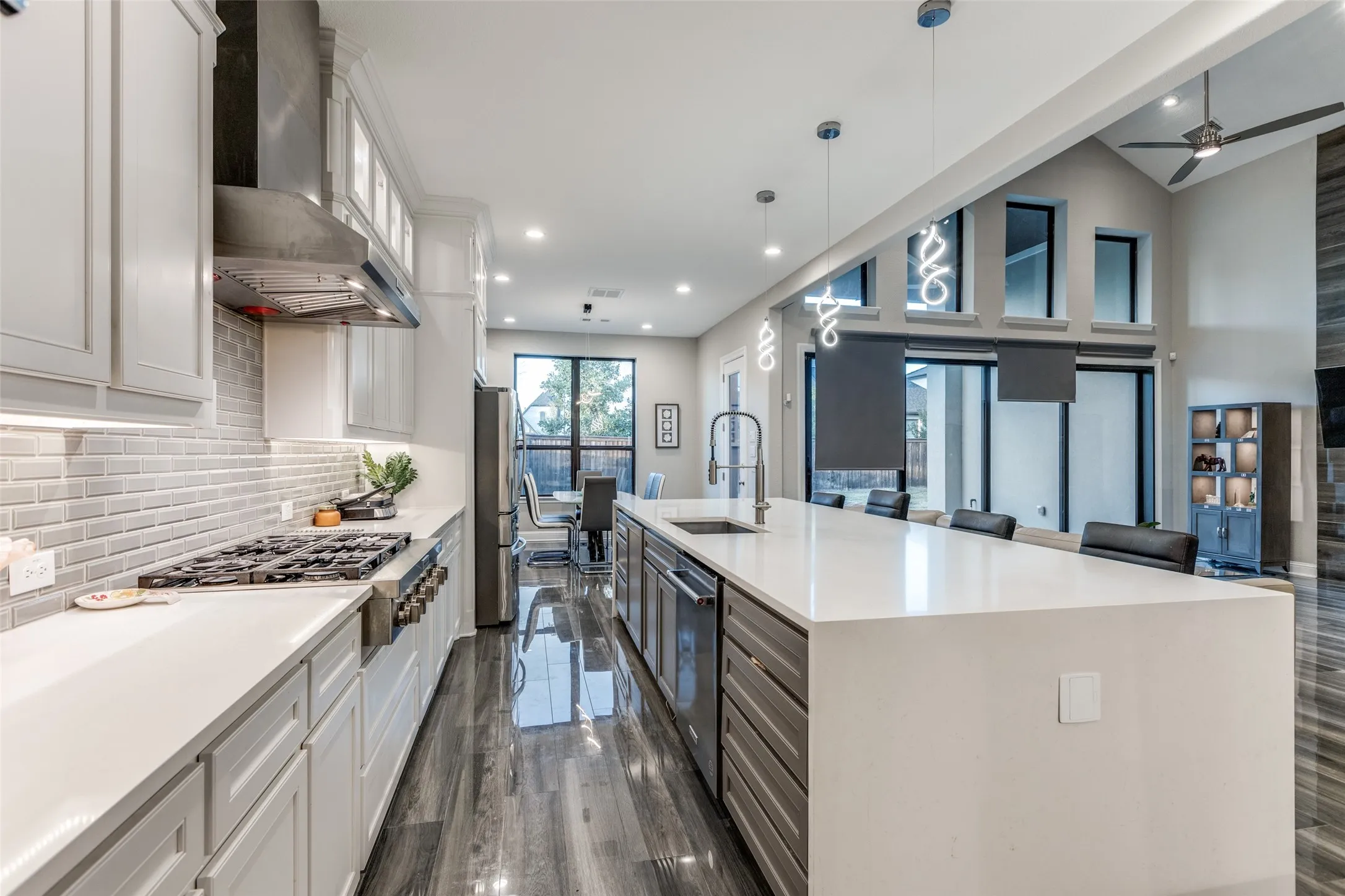 Open-concept kitchen featuring an expansive island with seating, a gas range with a stainless steel vent hood, light gray subway tile backsplash, white shaker cabinetry, and wood-finish flooring