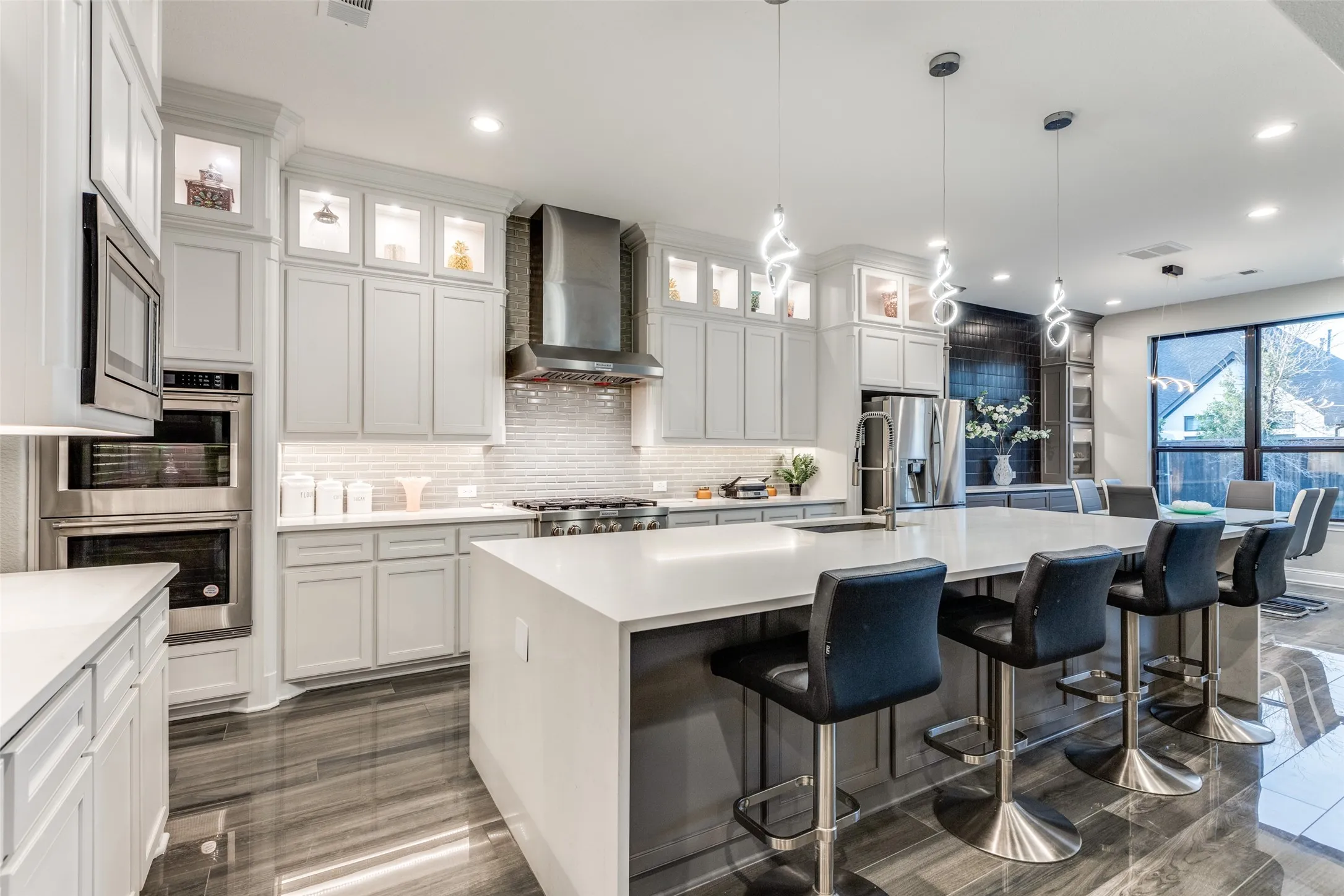 Gourmet kitchen featuring a large central island with seating, integrated stainless steel appliances, a tile backsplash, light cabinetry, and contemporary pendant lighting