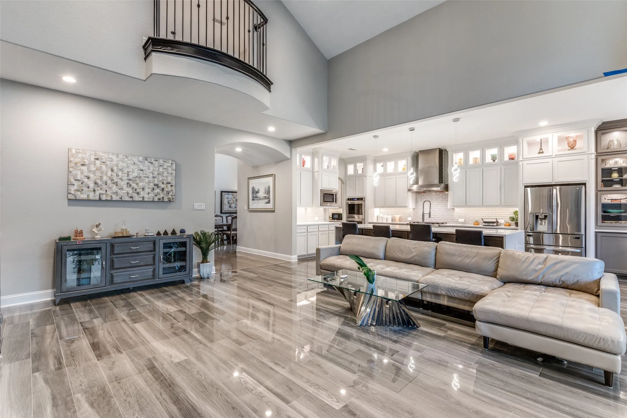 Open-concept living area with soaring ceilings, wood-finish flooring, a contemporary kitchen, a breakfast bar, and a second-story balcony with an iron railing