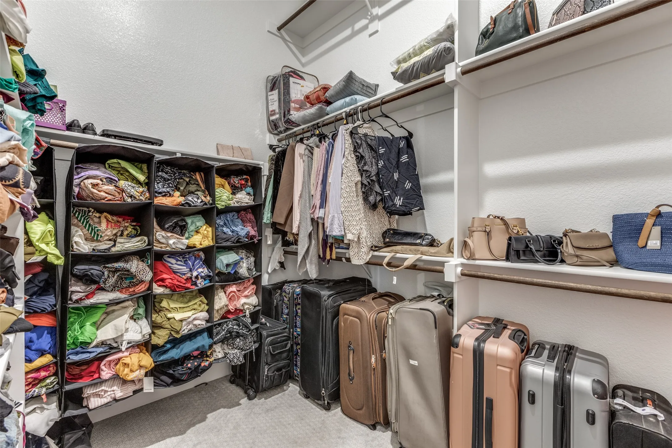 Walk-in closet featuring white built-in shelving, multiple hanging rods, and textured wall finishes
