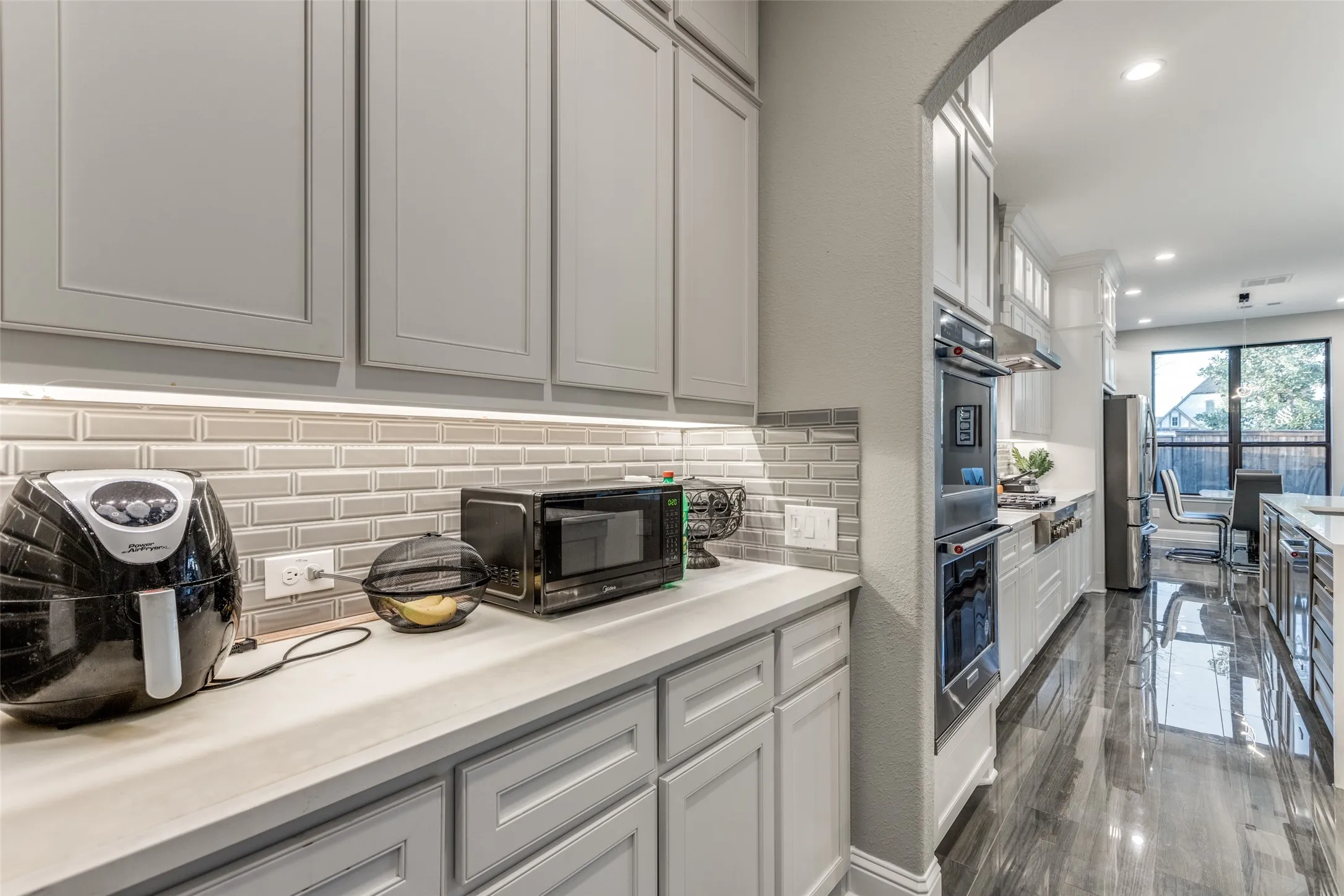 Kitchen featuring light gray cabinetry, subway tile backsplash, under-cabinet lighting, double wall ovens, and wood-finish flooring