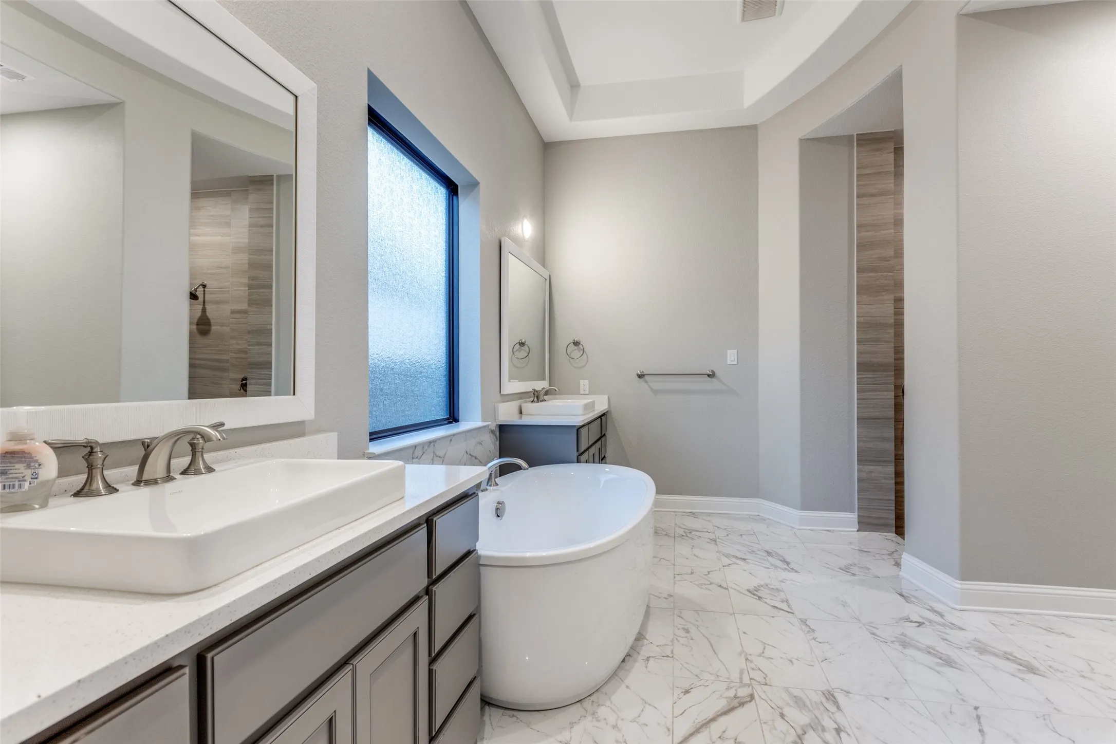 Freestanding soaking tub centered on marble-look tile flooring