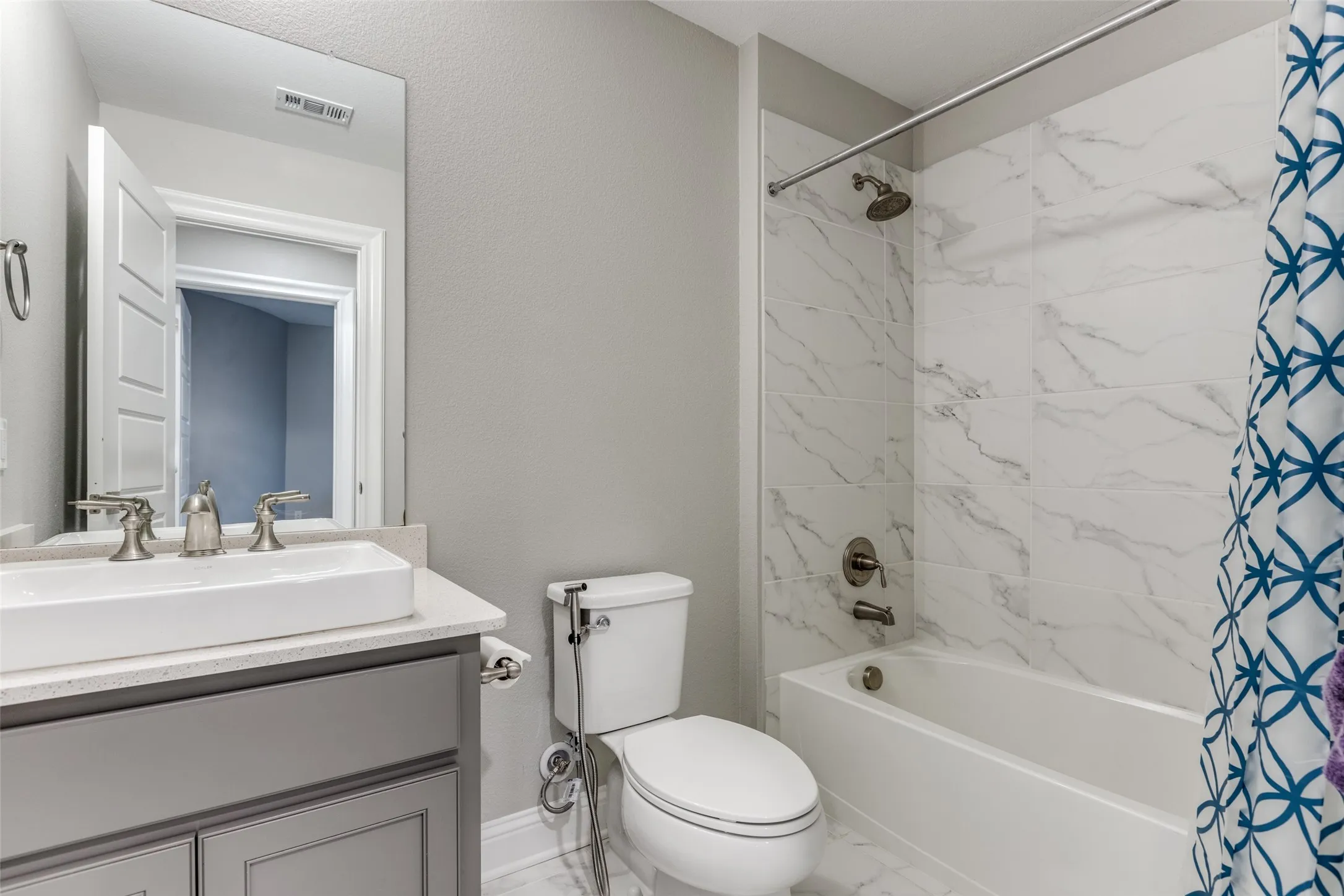 Bathroom featuring a white rectangular vessel sink, brushed nickel faucet, light gray vanity with built-in storage, a white toilet, and a bathtub with white marble-patterned tile surround