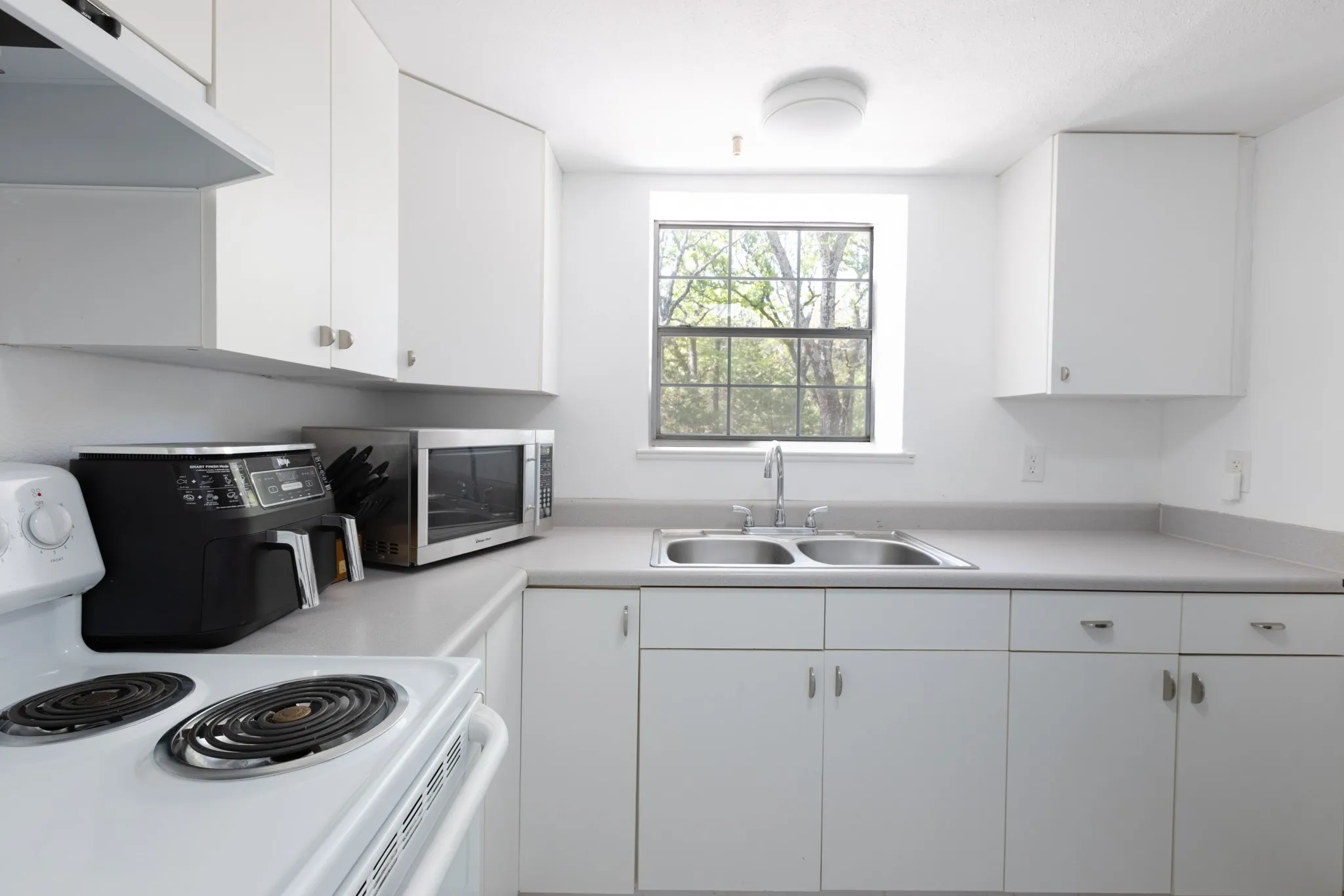 Guest house kitchen with electric stove, double stainless sinks, and refrigerator.