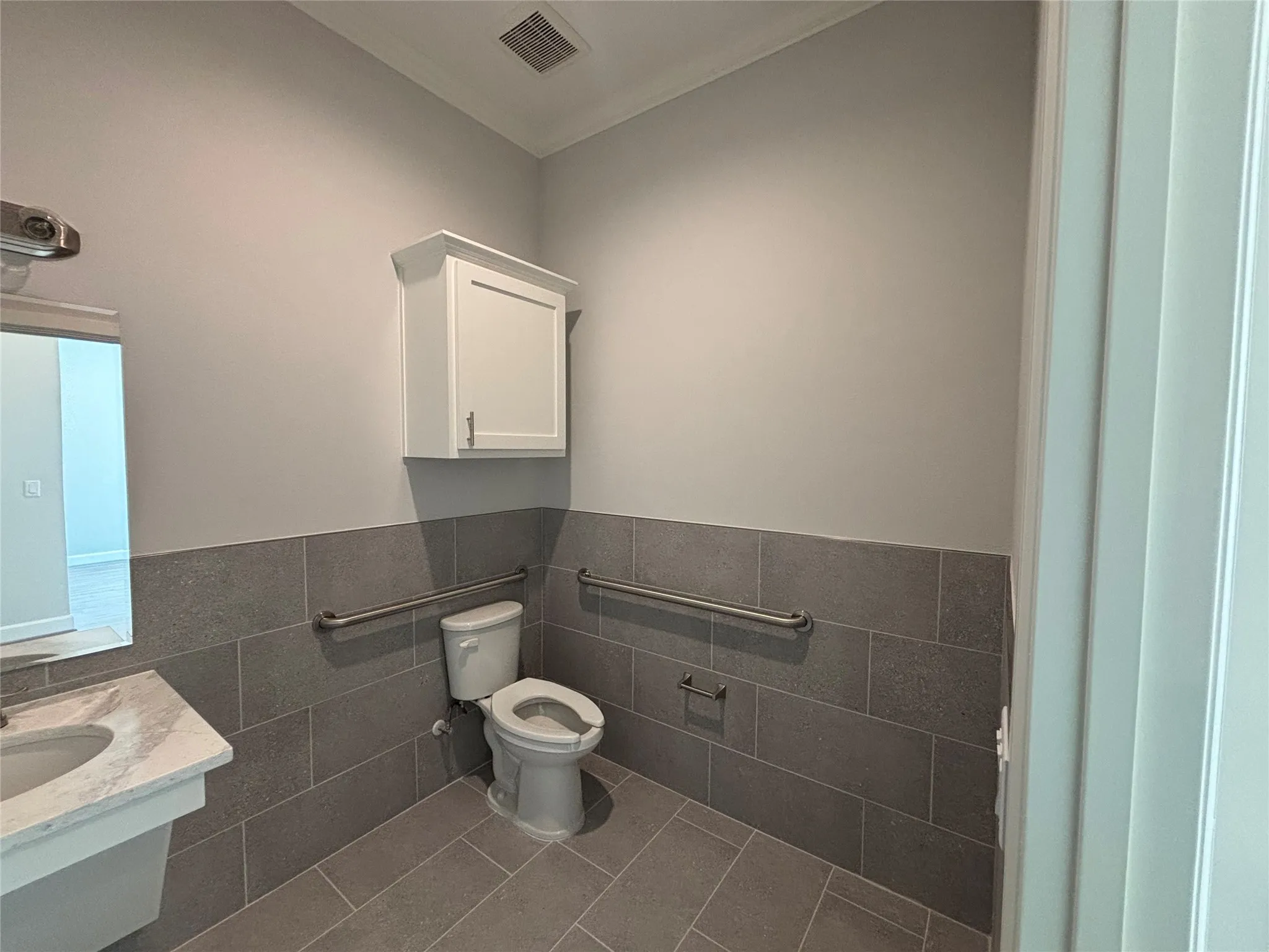 Bathroom featuring large-format gray floor and wall tile, a white wall-mounted cabinet, and a pedestal sink with a white stone countertop