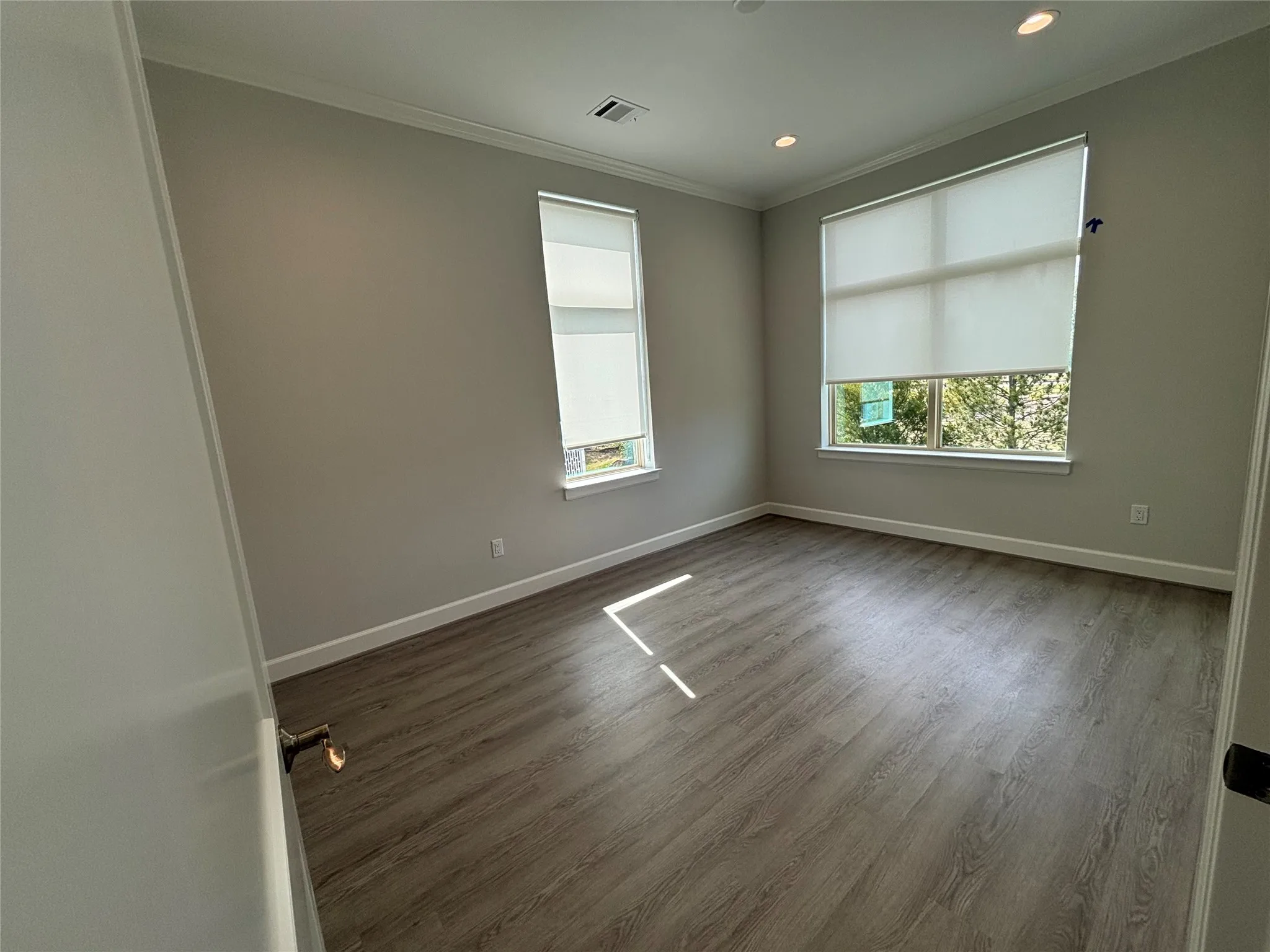 Neutral-toned room featuring two windows with roller shades, wood-finish flooring, recessed lighting, and crown molding