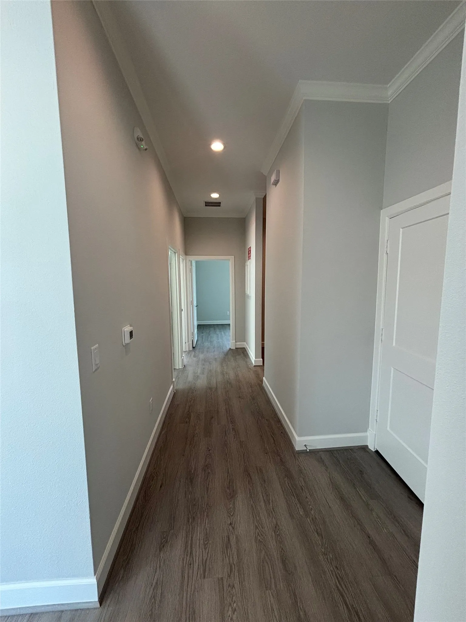 Hallway featuring wood-finish flooring, recessed lighting, crown molding, and white interior doors