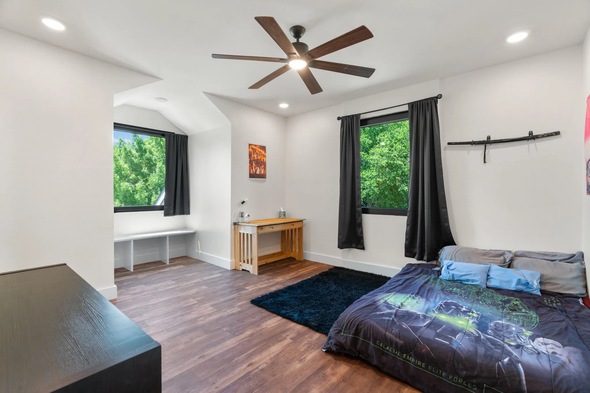 Spacious room featuring wood-finish flooring, two windows with black frames, recessed lighting, and a ceiling fan