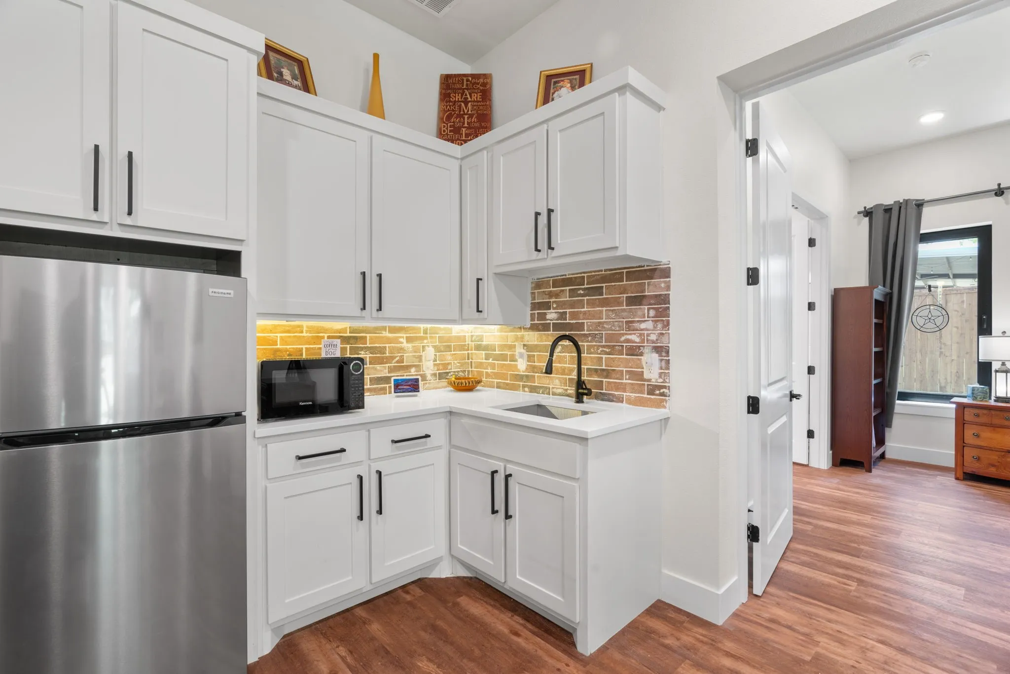 Compact kitchen area featuring white shaker cabinetry, stainless steel appliances, and a brick-patterned backsplash