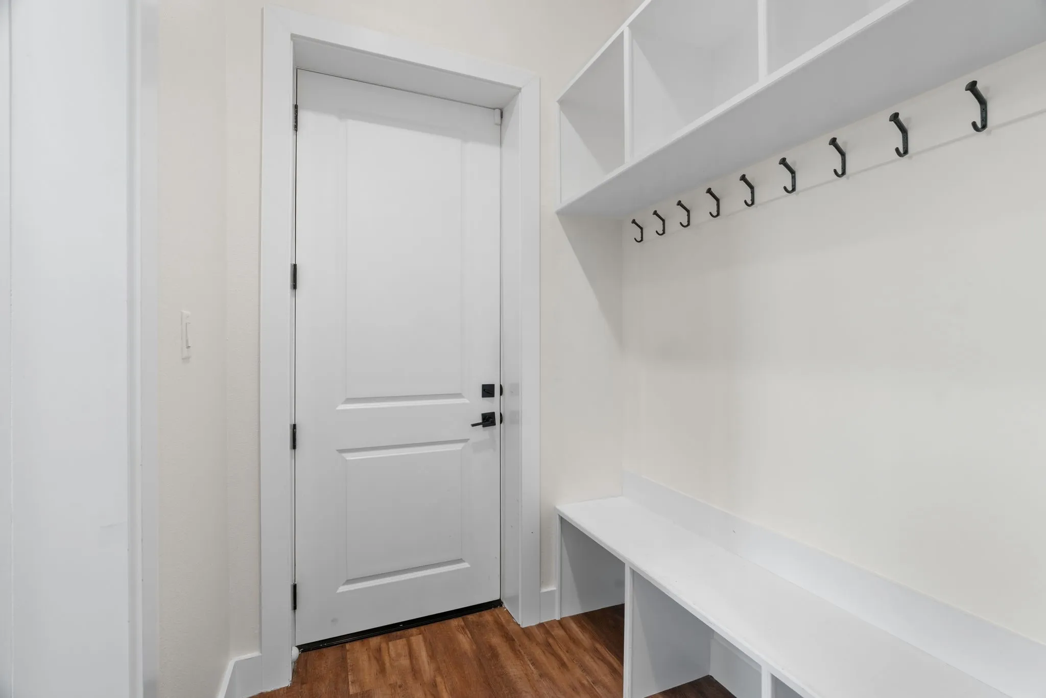 Mudroom featuring built-in white shelving, integrated bench seating, and multiple coat hooks