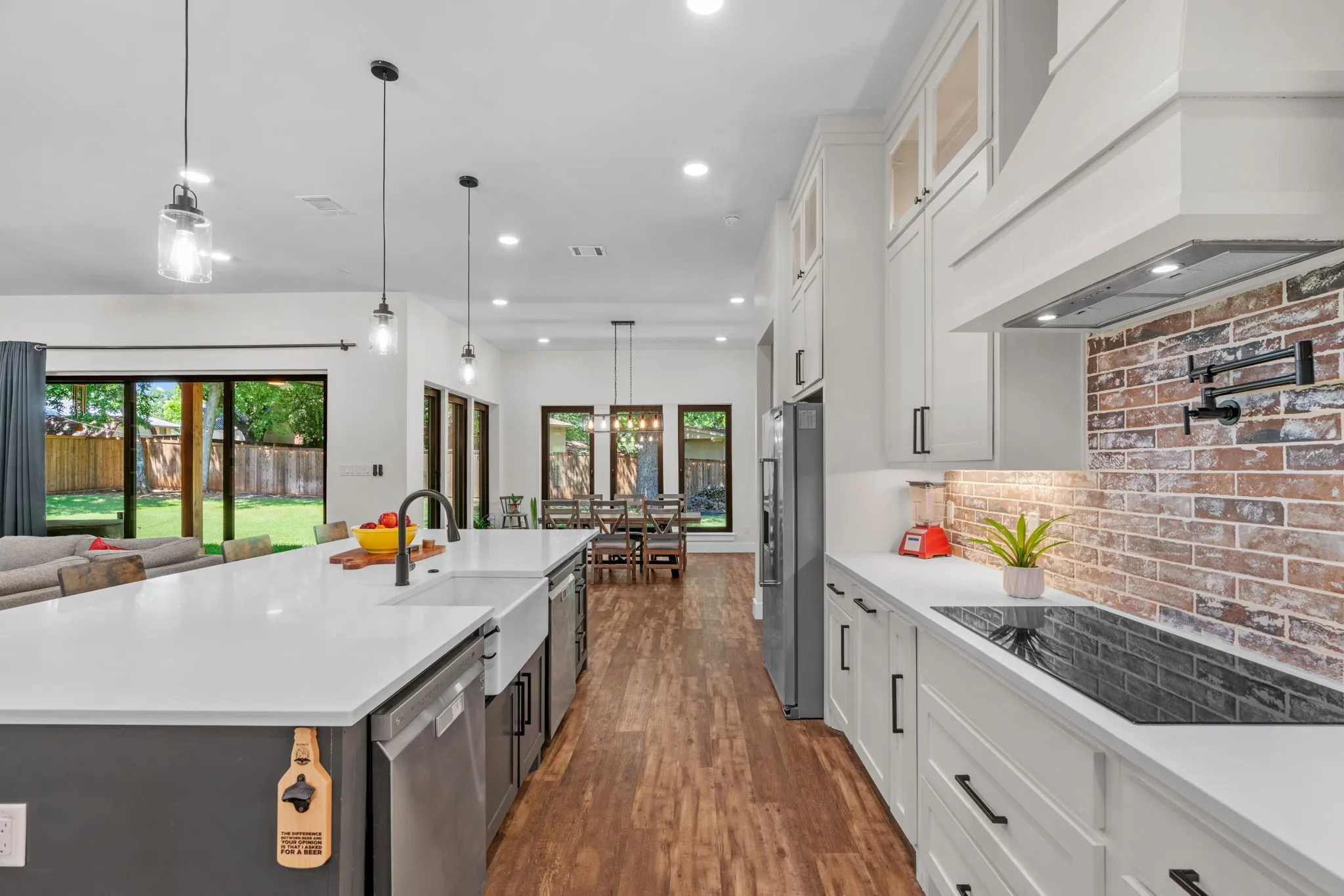 Gourmet kitchen featuring a large central island with a farmhouse sink, stainless steel appliances, a brick-finish backsplash, white cabinetry, and wood-finish flooring