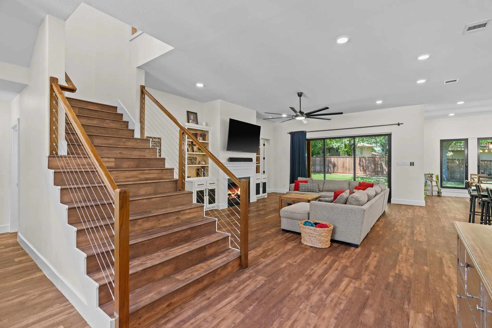 Wood-finish staircase with cable railing, complemented by wood-finish flooring throughout the open-concept living area