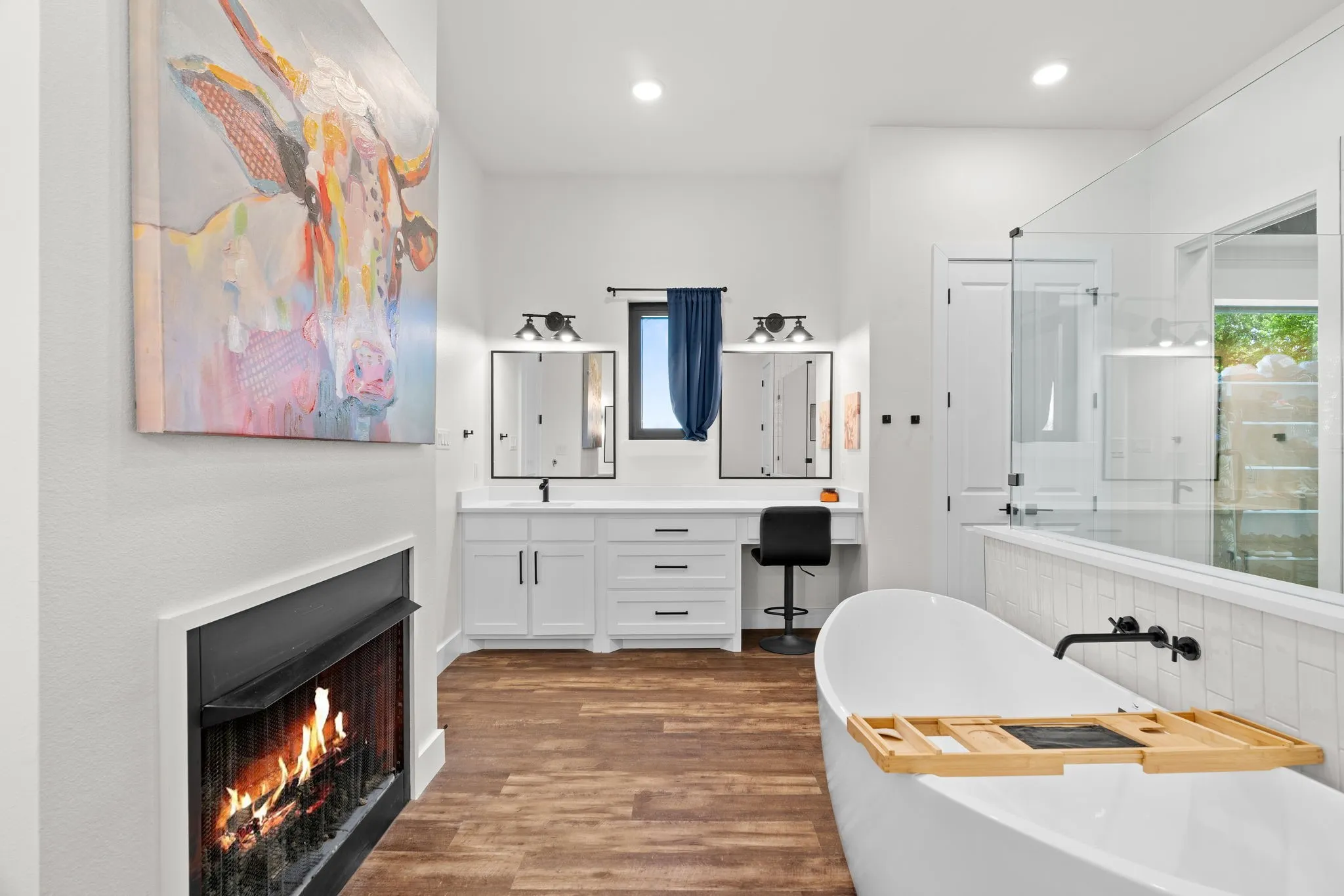 Freestanding soaking tub with wall-mounted matte black faucet, alongside a dual vanity with white cabinetry and dark hardware