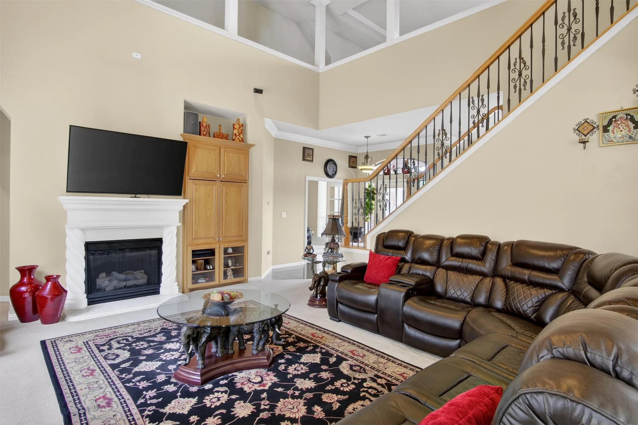 Living area featuring a fireplace with a white mantel, built-in wooden cabinetry, a grand staircase with wrought iron balusters, and a high vaulted ceiling with exposed beams