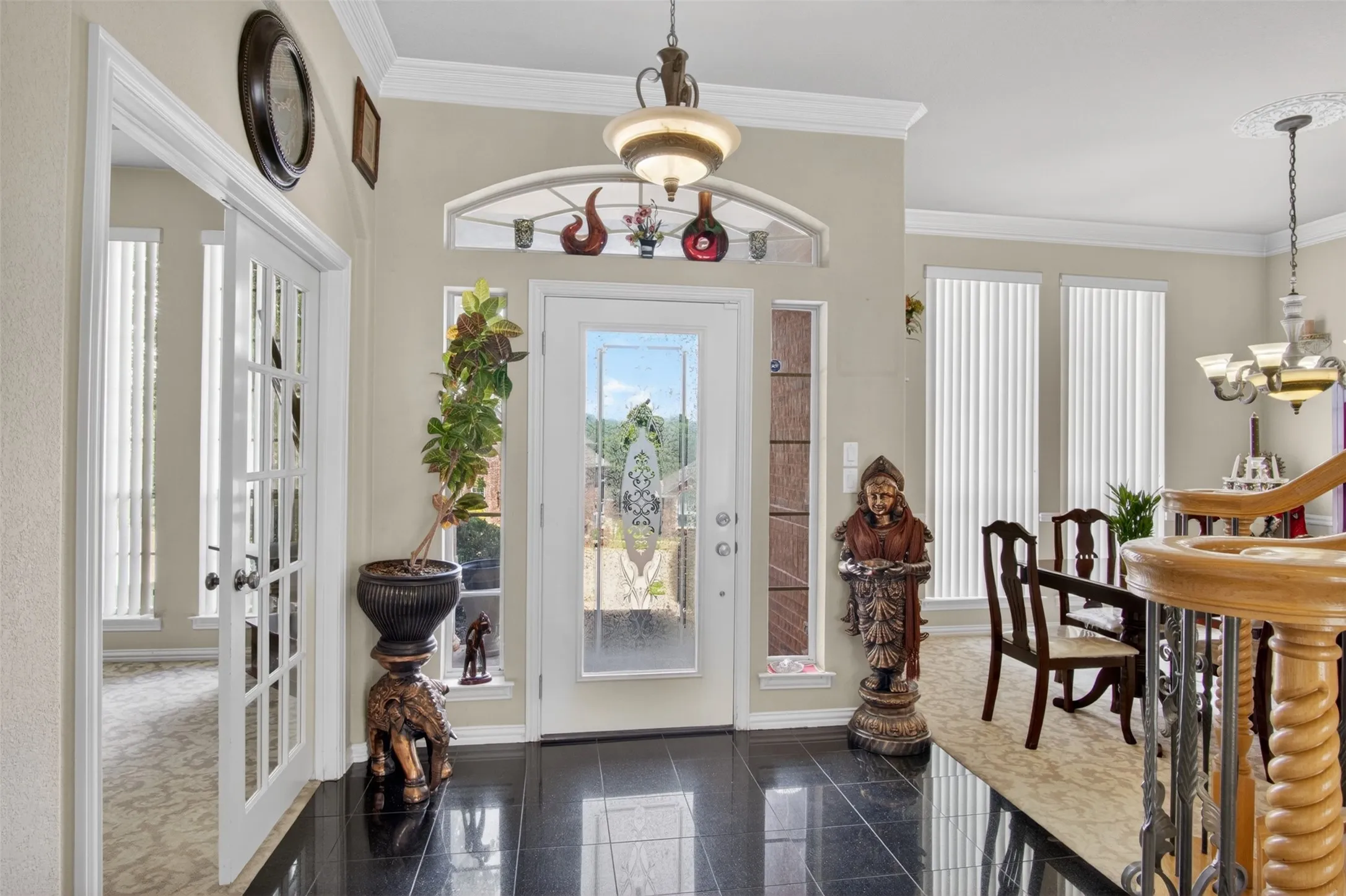 Entryway featuring polished black tile flooring, a decorative glass-paneled front door with an arched transom, and crown molding