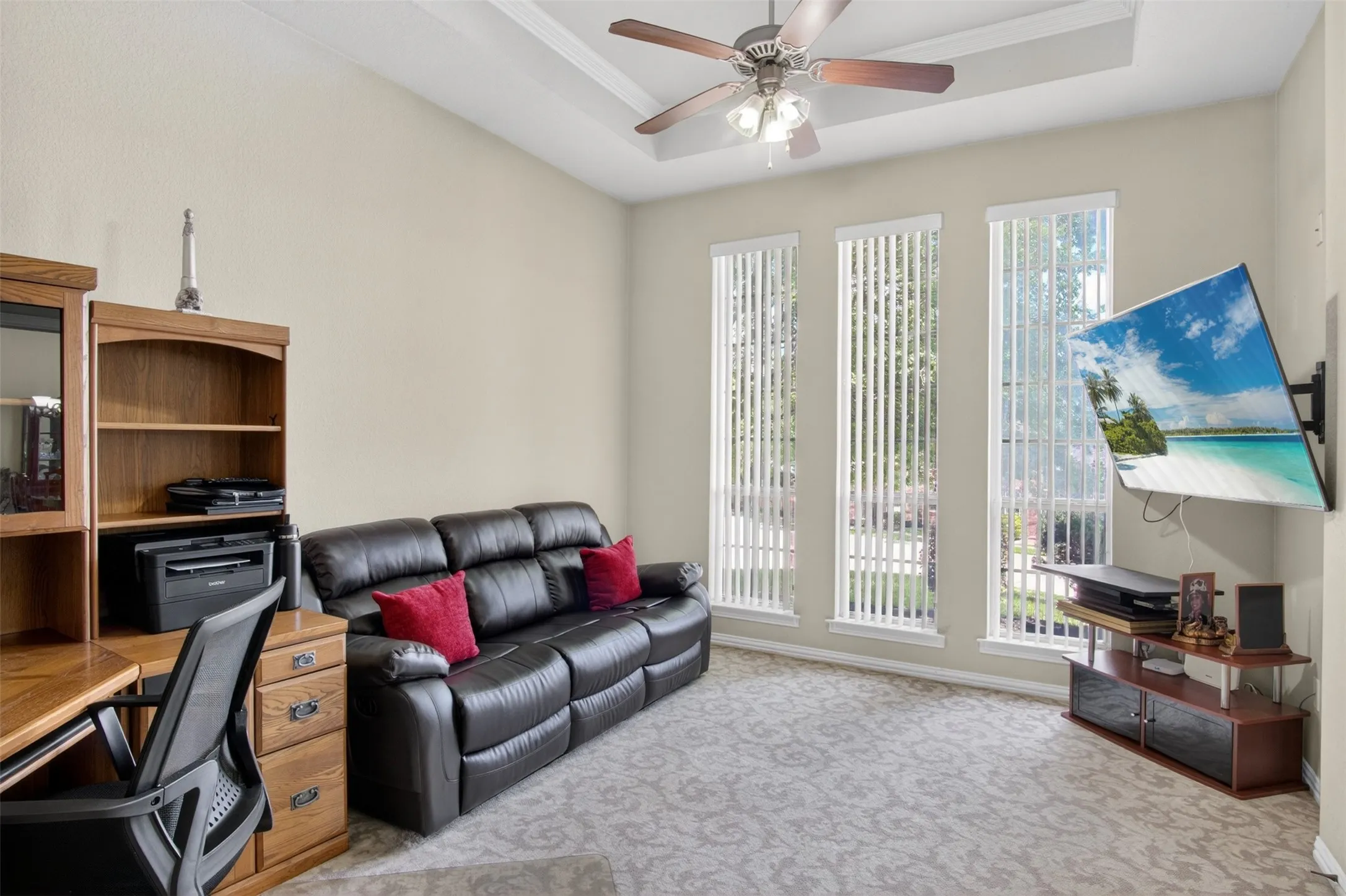Room featuring a tray ceiling with a ceiling fan, three tall windows with vertical blinds, and patterned carpeting