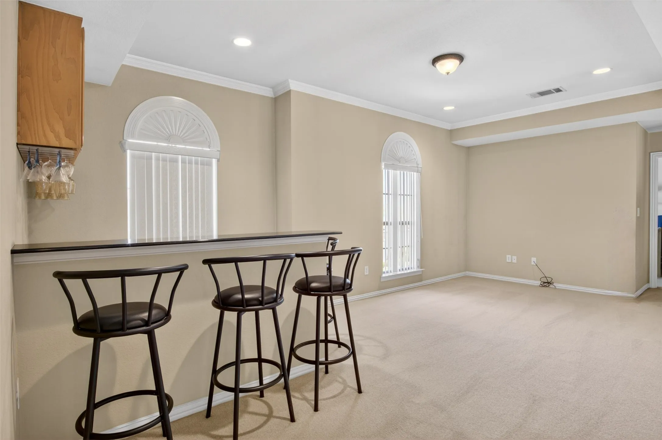 Carpeted entertainment space featuring a built-in bar with a dark countertop and an overhead wood-finish cabinet with stemware storage