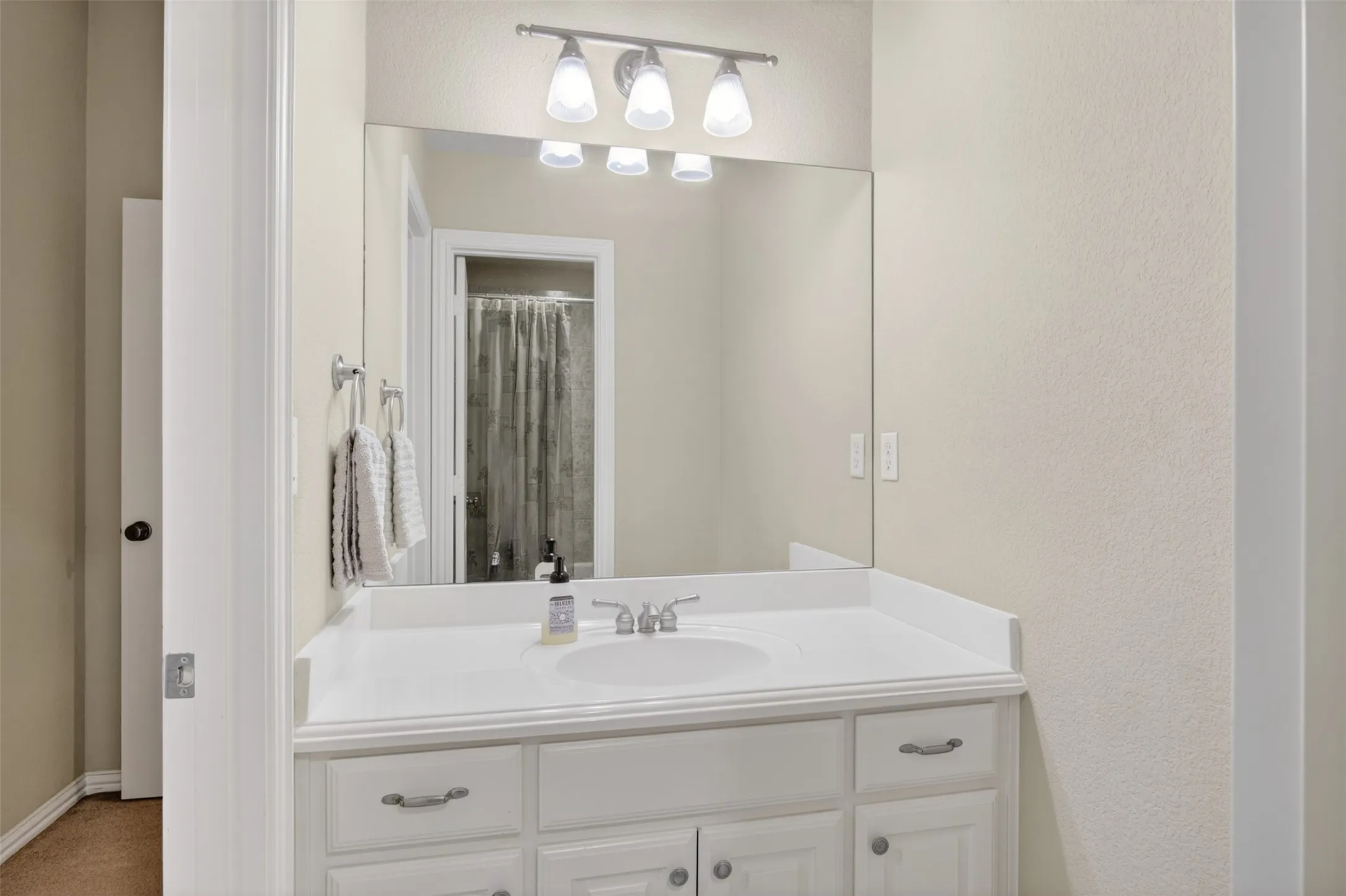 Bathroom vanity featuring a white countertop with an integrated sink, brushed nickel faucet, and a wall-mounted rectangular mirror