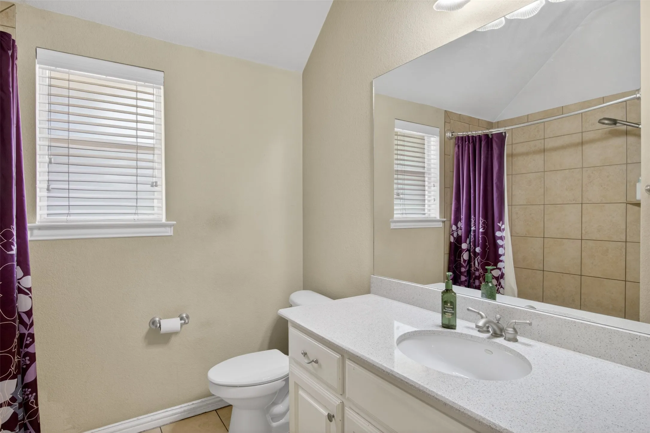 Bathroom featuring a single vanity with an integrated sink, a large wall-mounted mirror, and a window with blinds