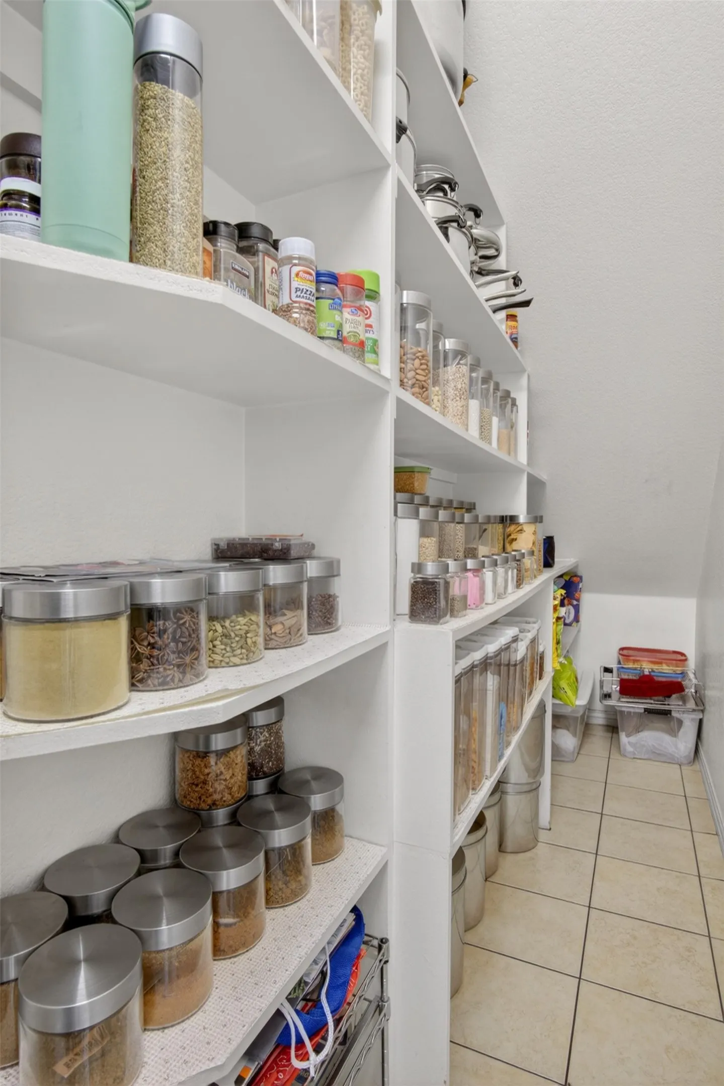 Spacious pantry featuring extensive built-in shelving, tile flooring, and white painted walls