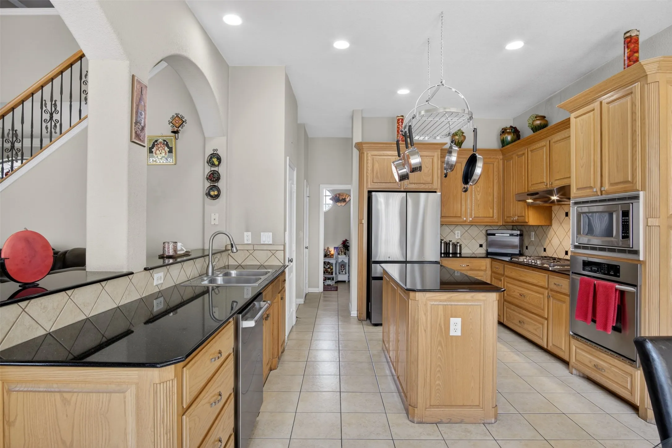 Kitchen featuring light wood cabinetry, black countertops, stainless steel appliances, a center island with additional counter space, and tile flooring