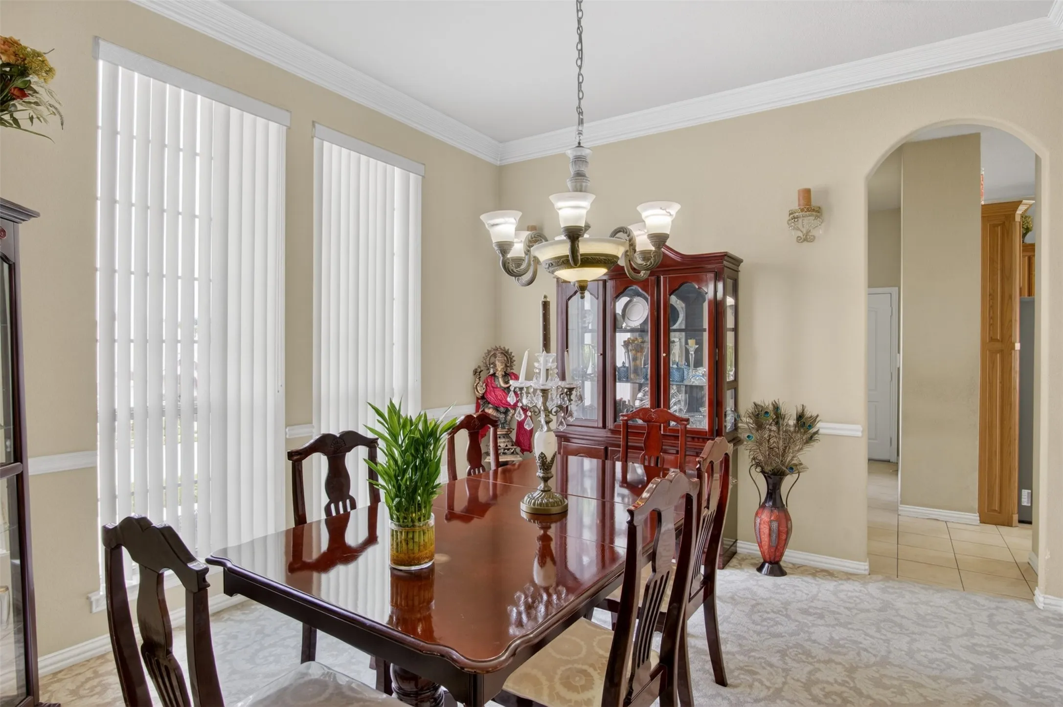 Dining space featuring elegant chandelier lighting, crown molding, chair rail detailing, two tall windows with vertical blinds, and an arched entry