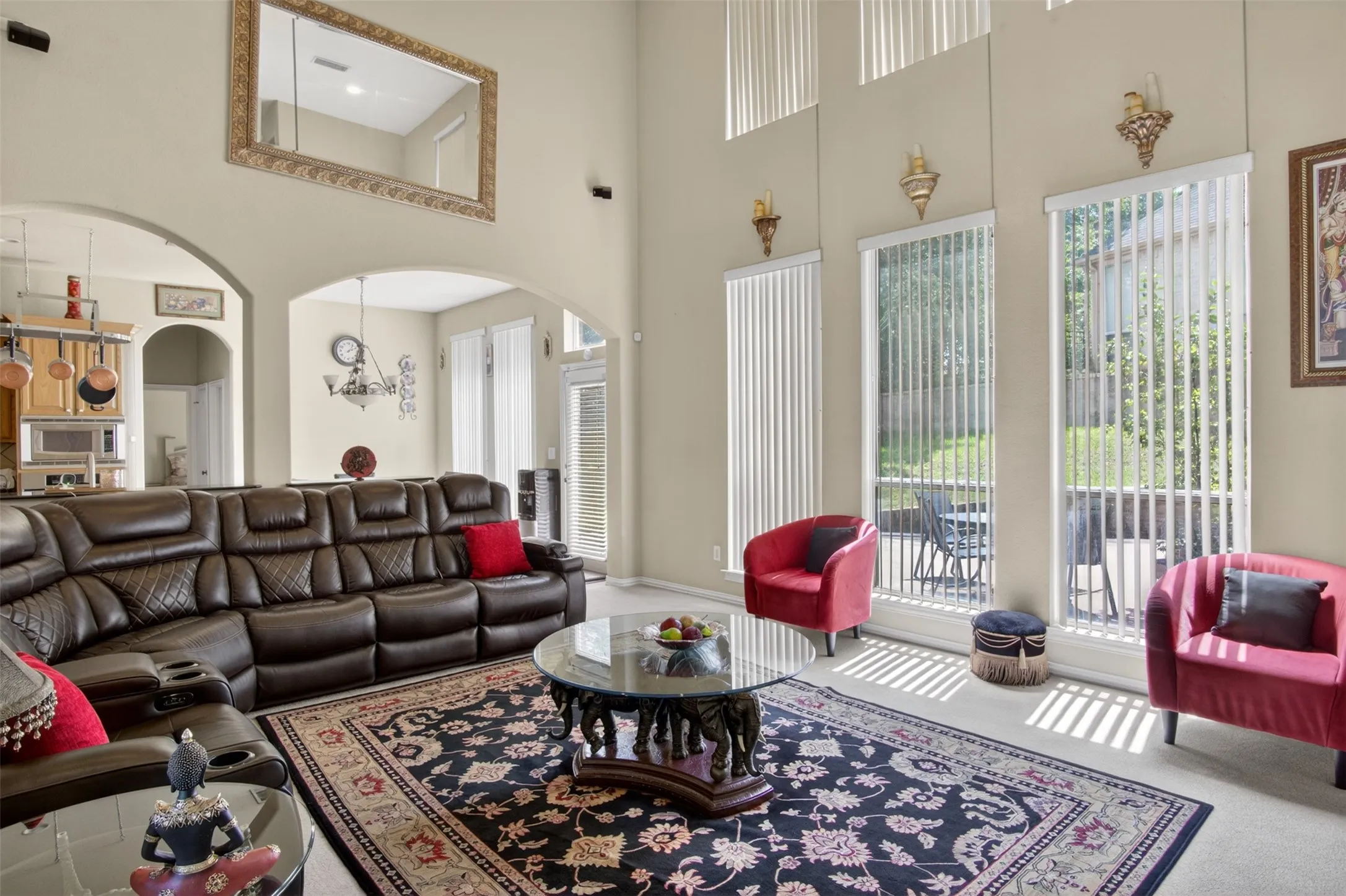 Living area featuring vaulted ceilings, arched doorways, a large mirror accent, and tall windows with vertical blinds