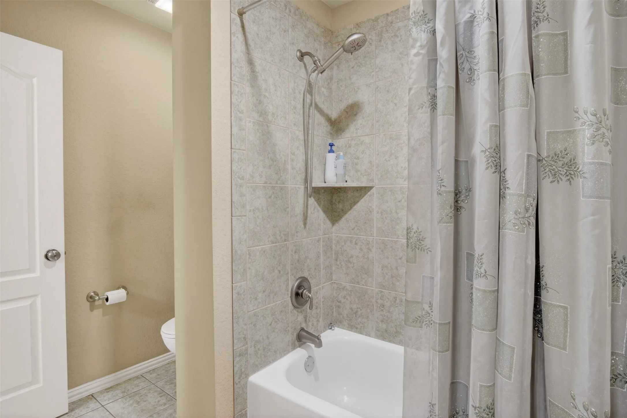 Bathtub with tiled surround, recessed shower niche, and brushed nickel fixtures