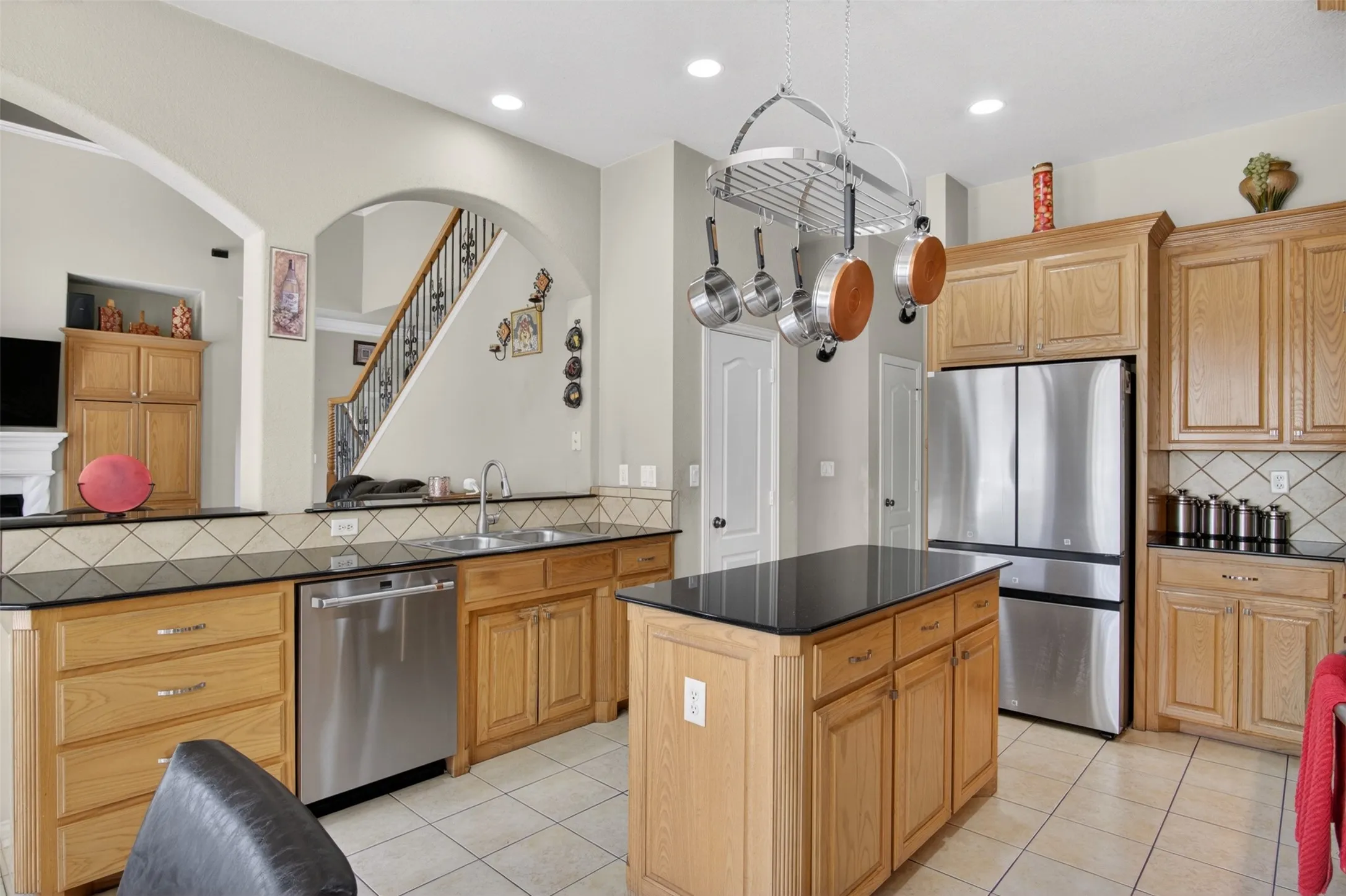 Kitchen featuring light wood cabinetry, black countertops, stainless steel appliances, and a central island with additional storage