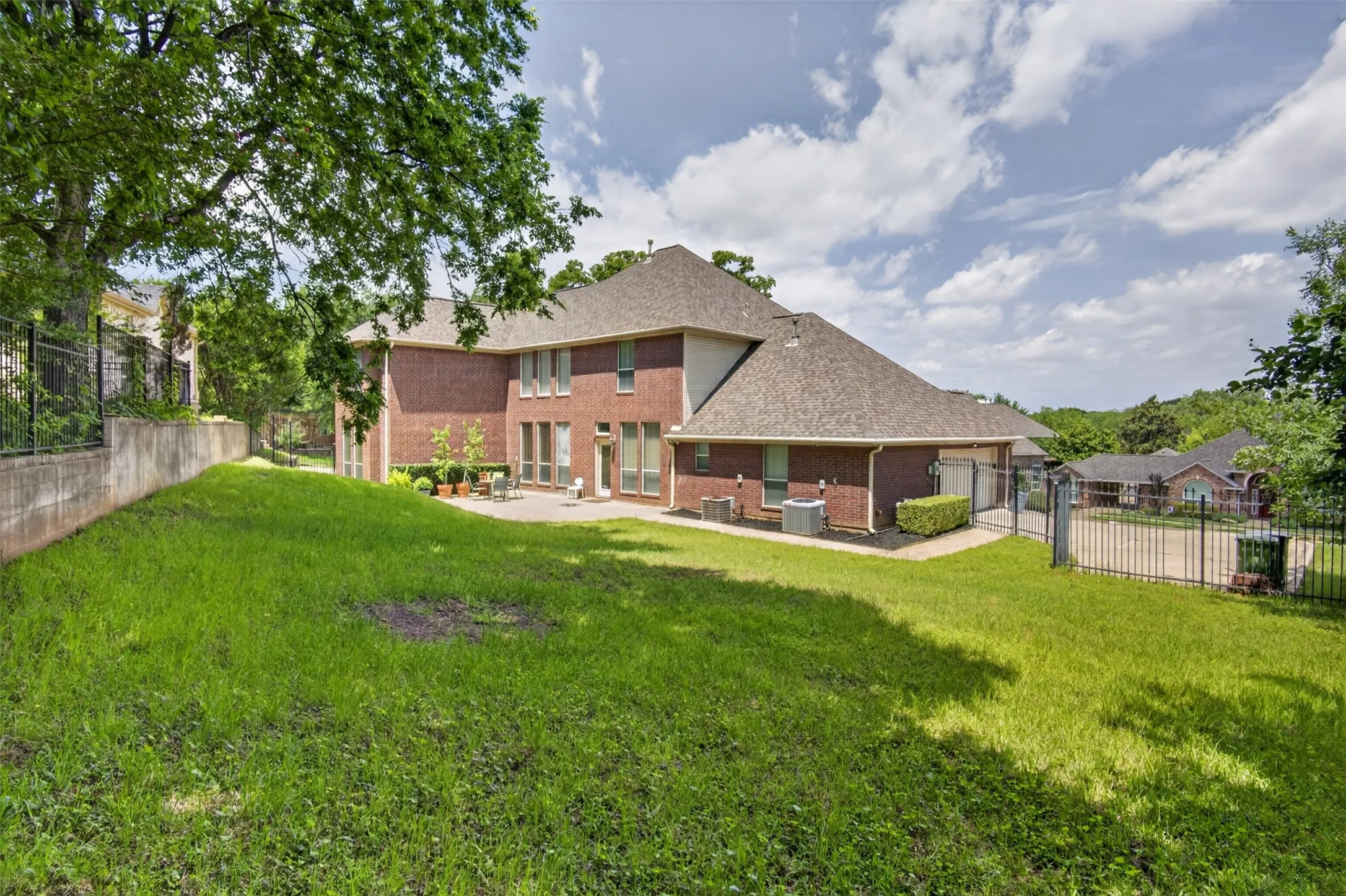 Expansive grassy yard with mature trees and a concrete retaining wall