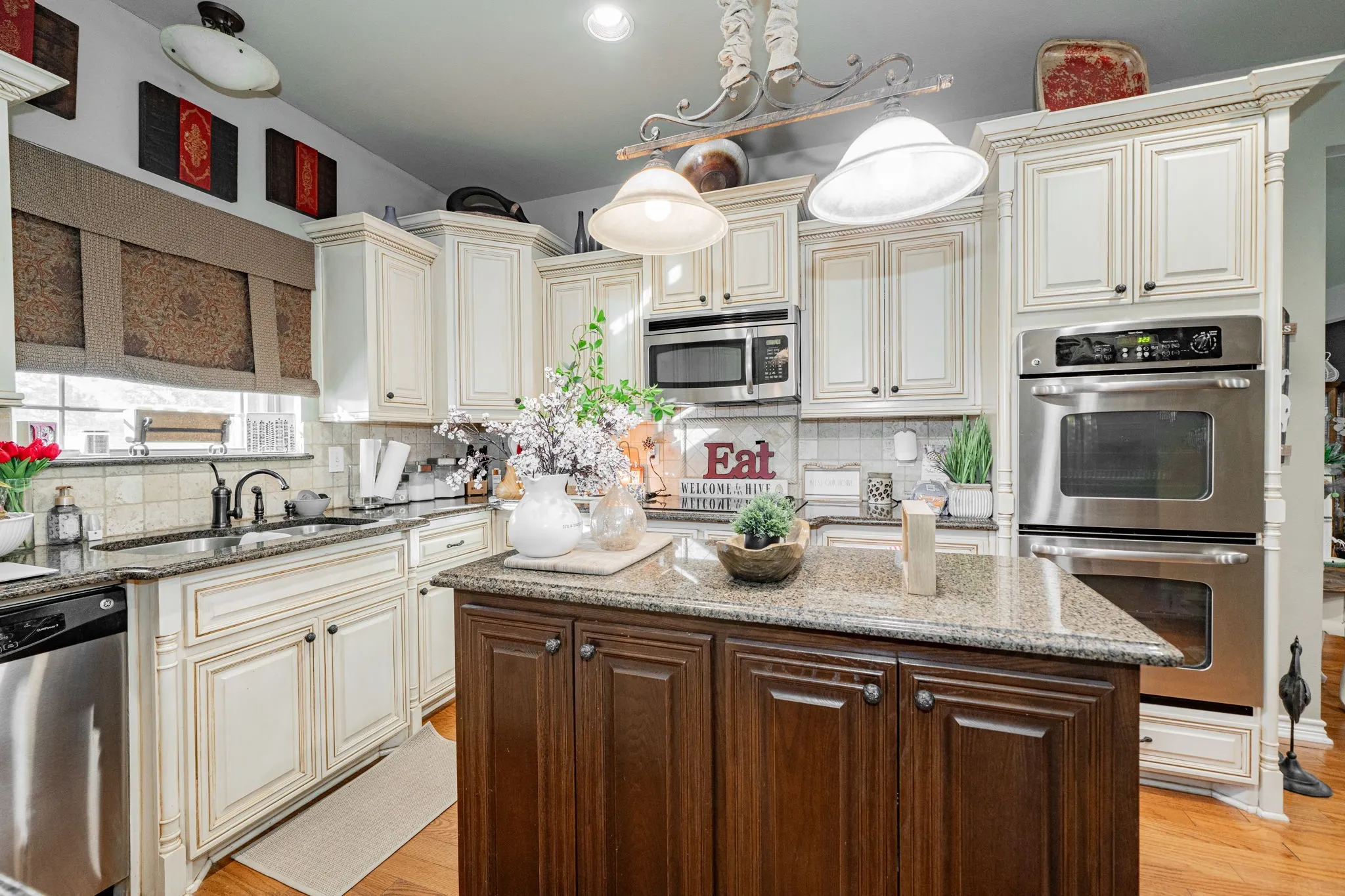 Gourmet kitchen featuring a central island with a stone-finish countertop, custom cabinetry, stainless steel appliances including a built-in double oven and microwave, and recessed lighting