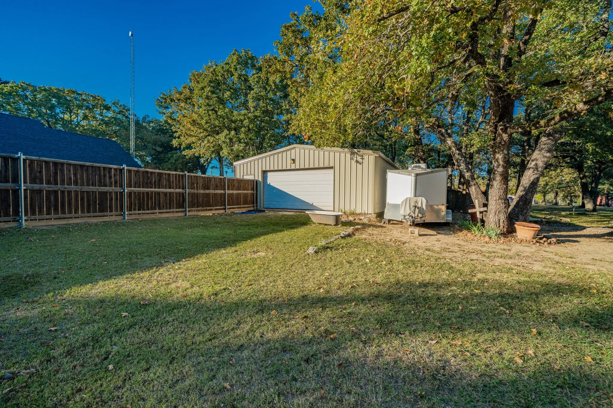 Expansive yard space featuring a metal outbuilding with a roll-up door, mature trees, and a wooden privacy fence