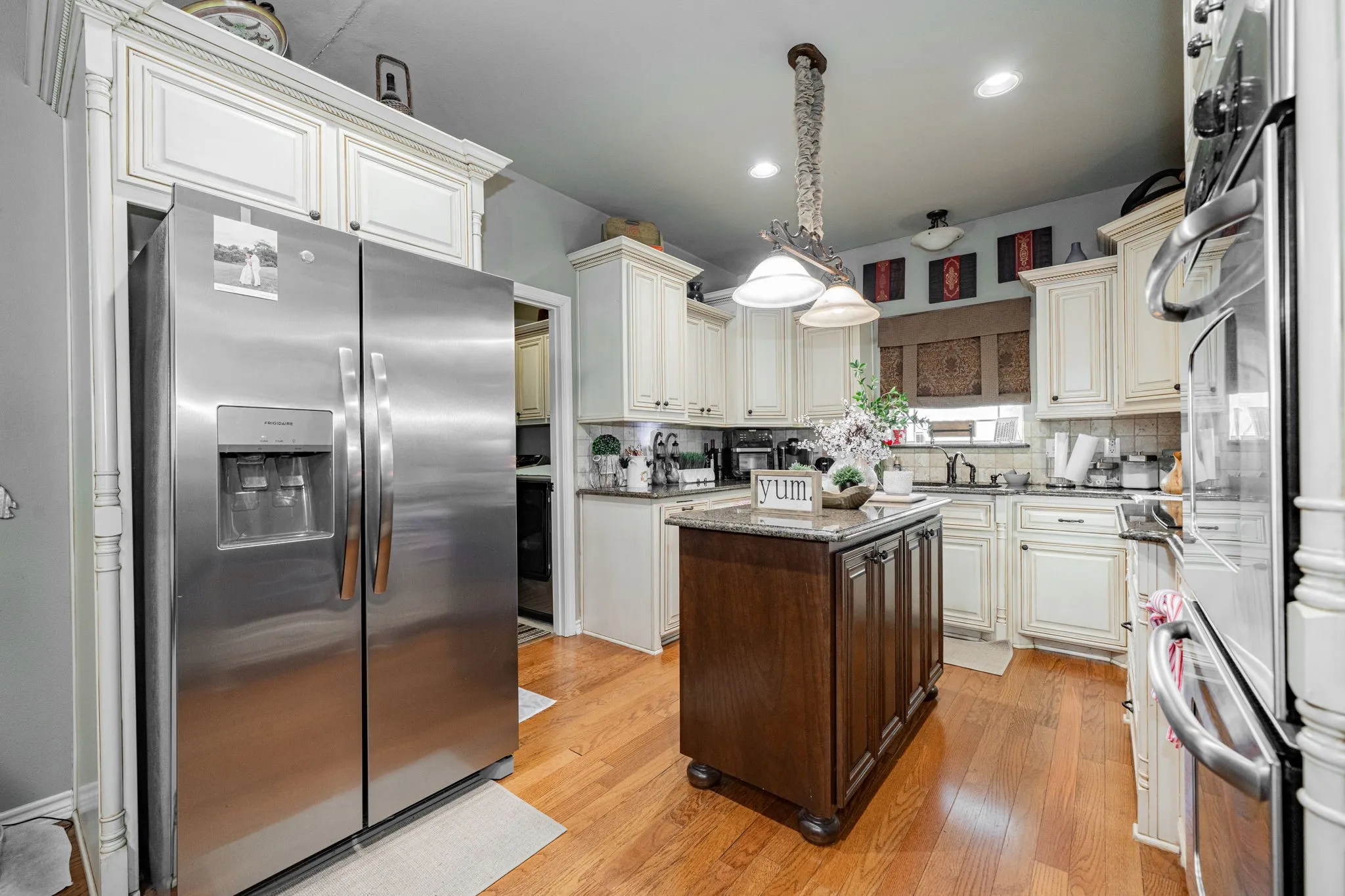 Spacious kitchen featuring wood-finish flooring, cream-toned cabinetry with dark hardware, a central island with a stone-finish countertop, and stainless steel appliances