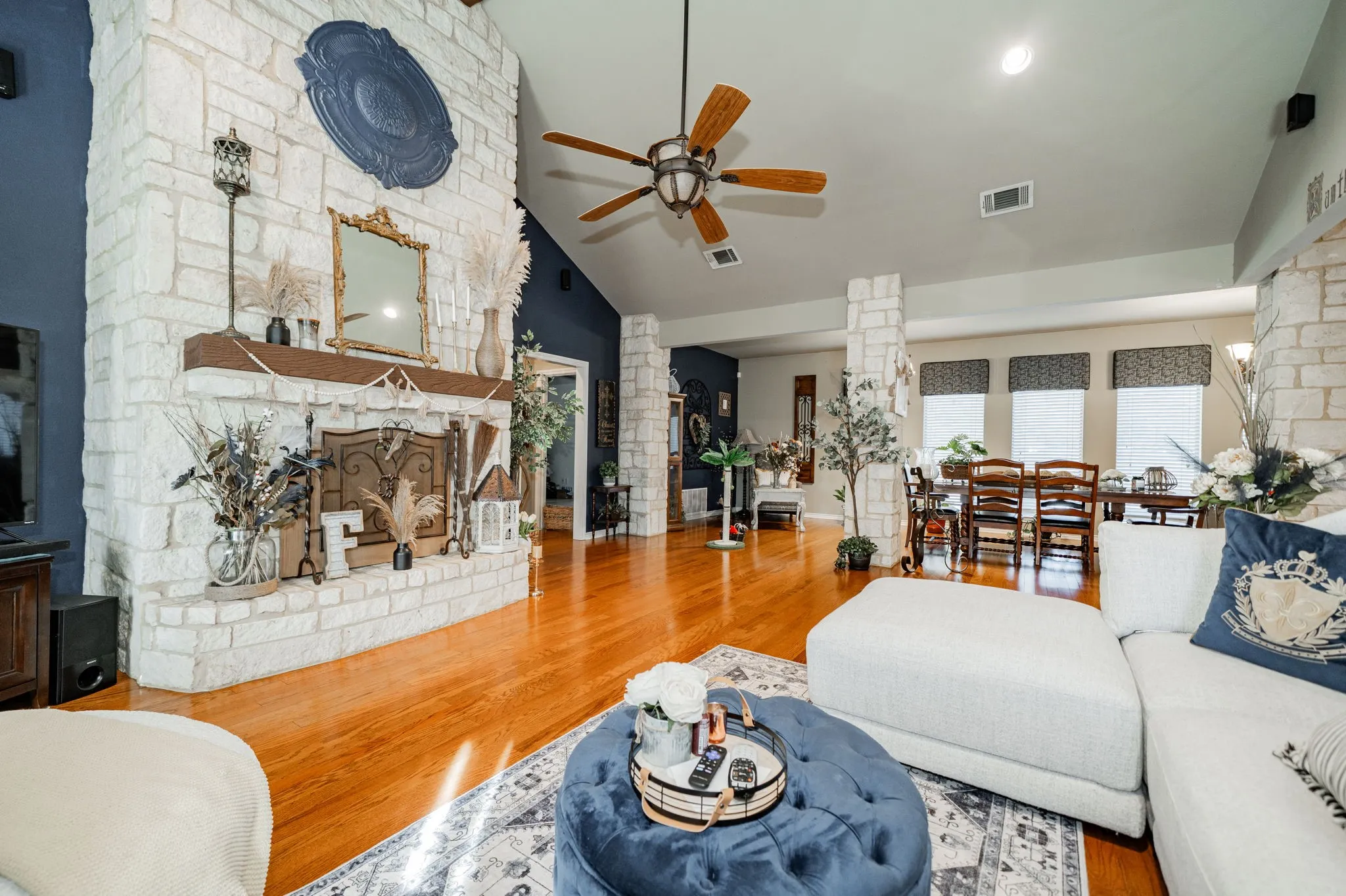 Stone-clad fireplace with a wood mantle, vaulted ceiling, wood-finish flooring, and a ceiling fan