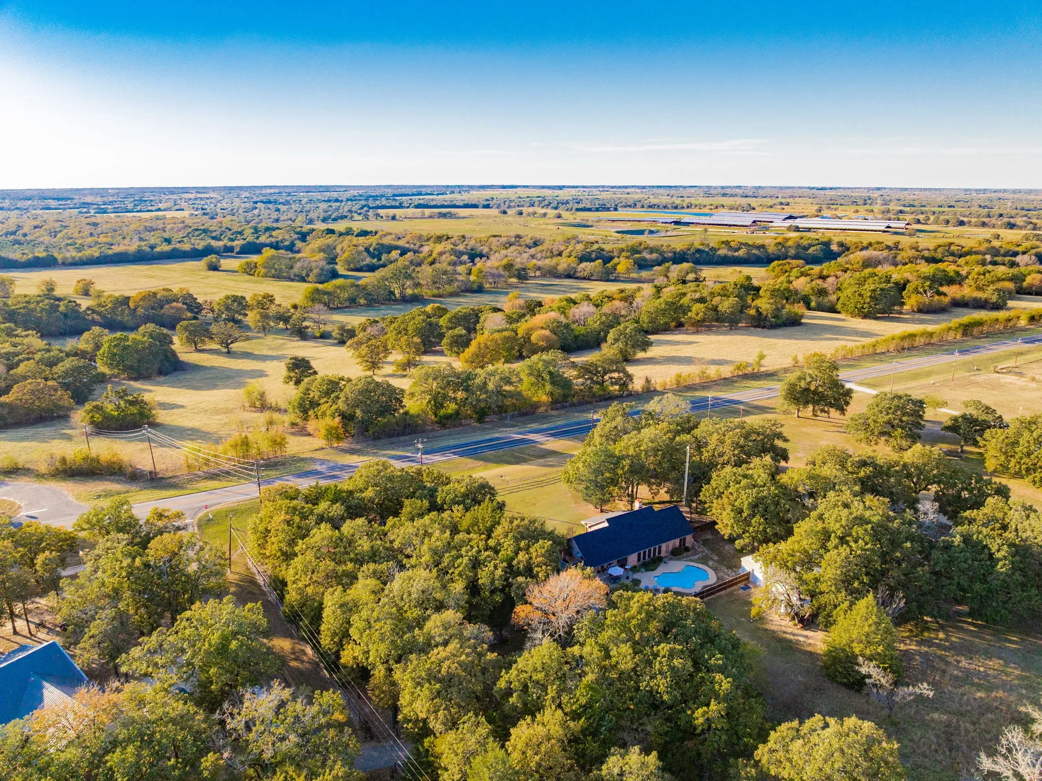 Ranch-style residence featuring a dark roof and a perimeter fence, surrounded by mature trees