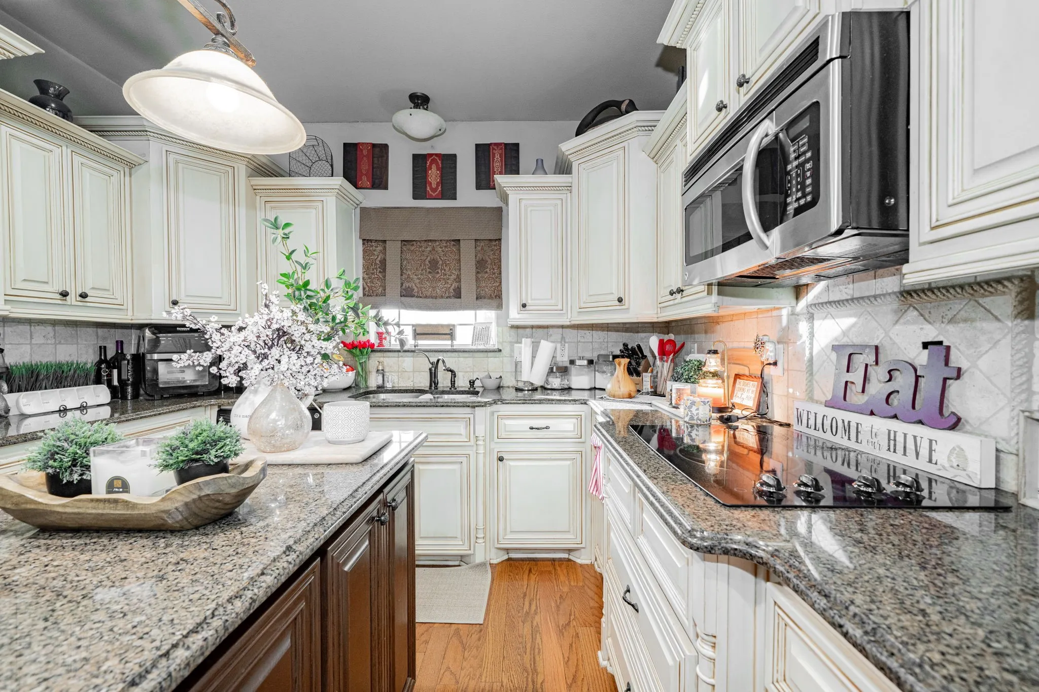 Kitchen featuring white paneled cabinetry with dark hardware, granite countertops, stainless steel microwave, and a black cooktop