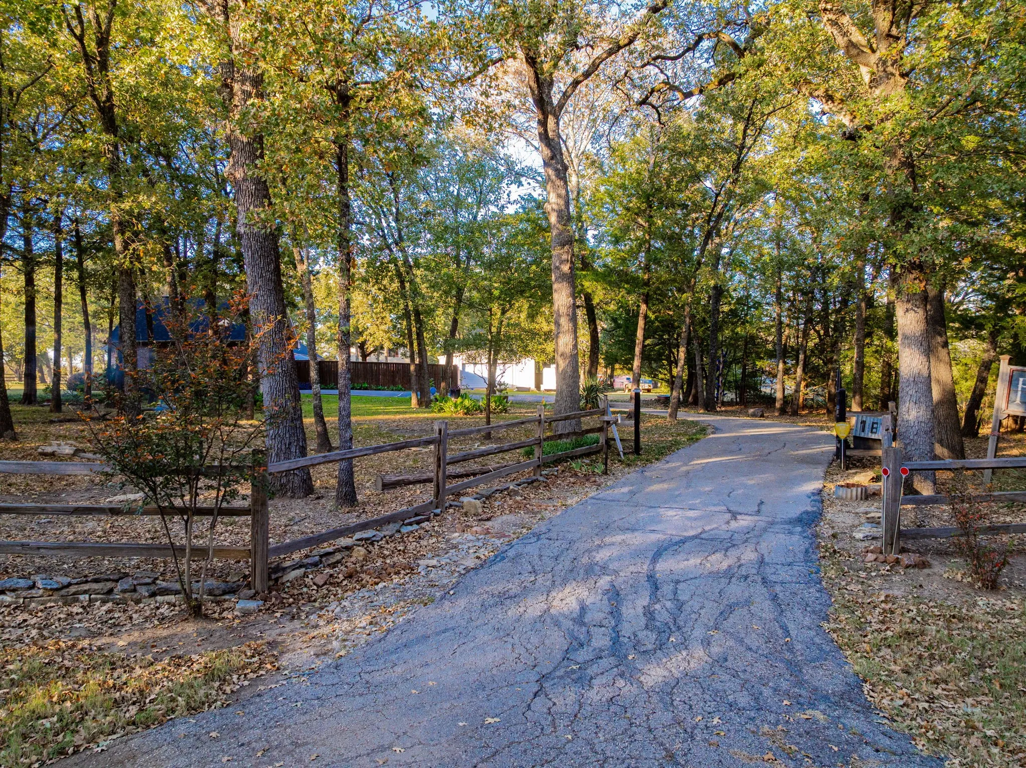 Paved driveway bordered by a split-rail fence and mature trees